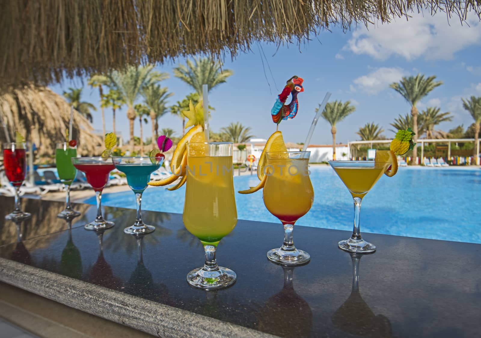 Several cocktail drinks by a tropical resort swimming pool