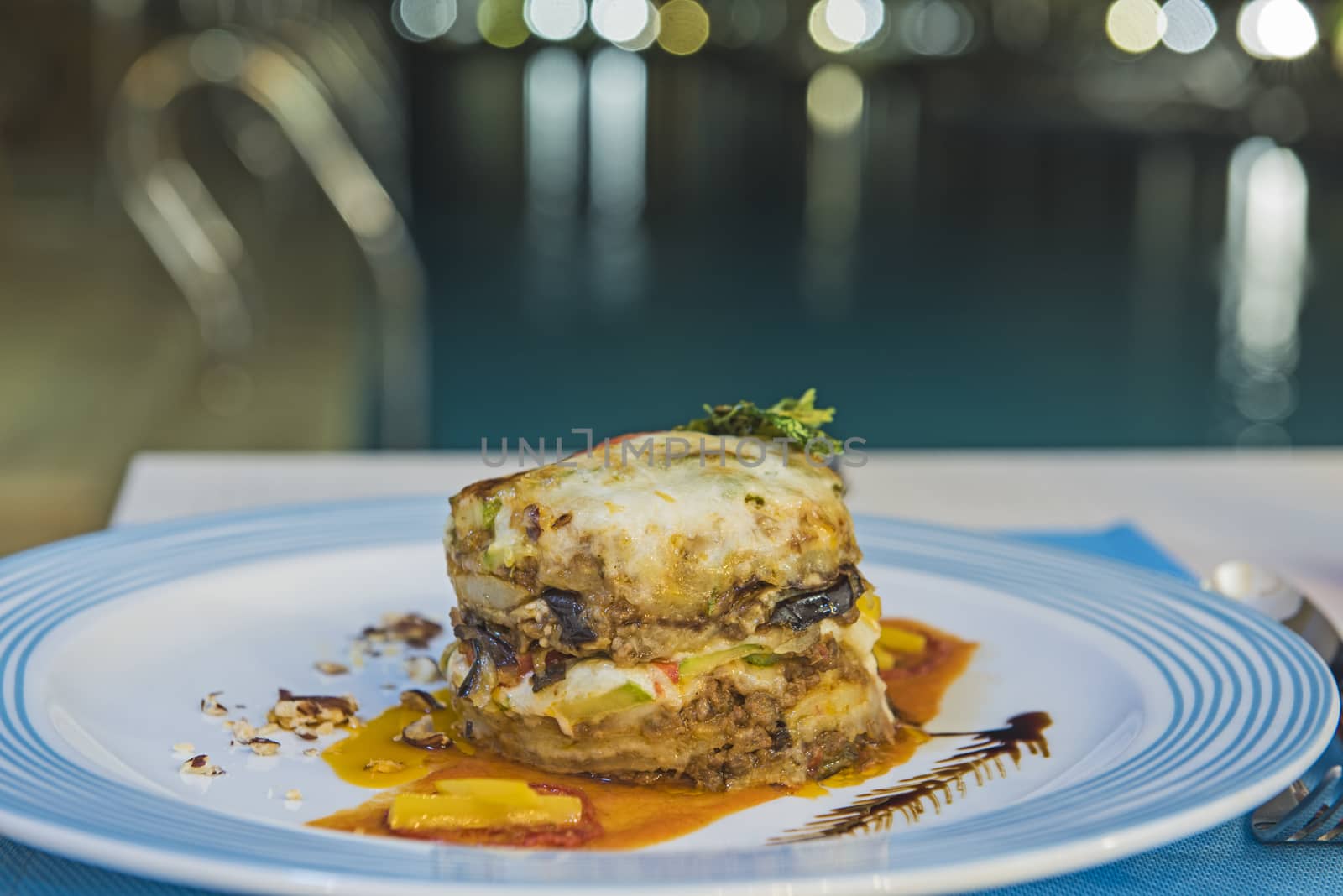 Greek moussaka a la carte meal on white plate at an outdoor restaurant by swimming pool