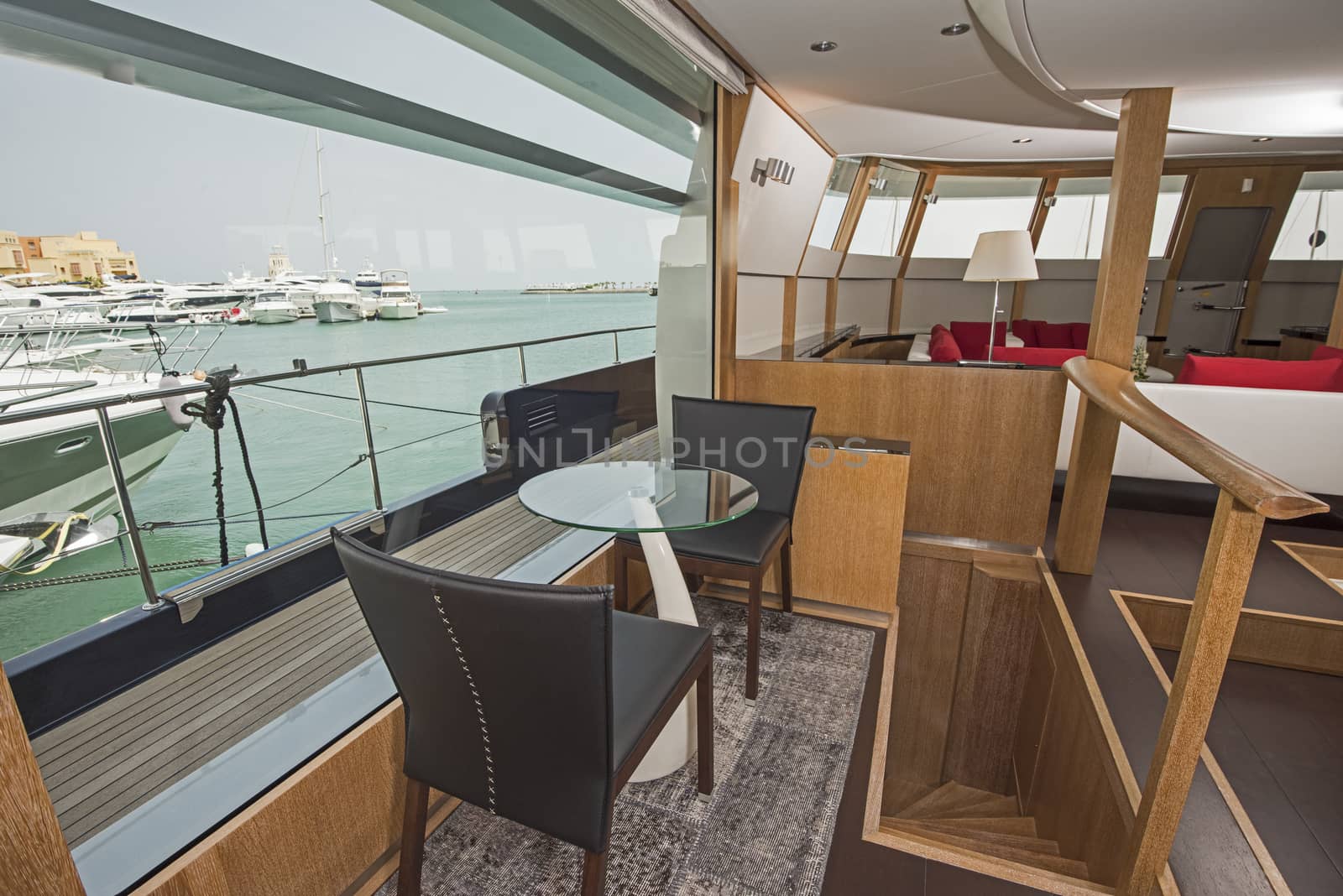 Seating in the salon area of a large luxury motor yacht with big panorama window showing view over tropical ocean marina