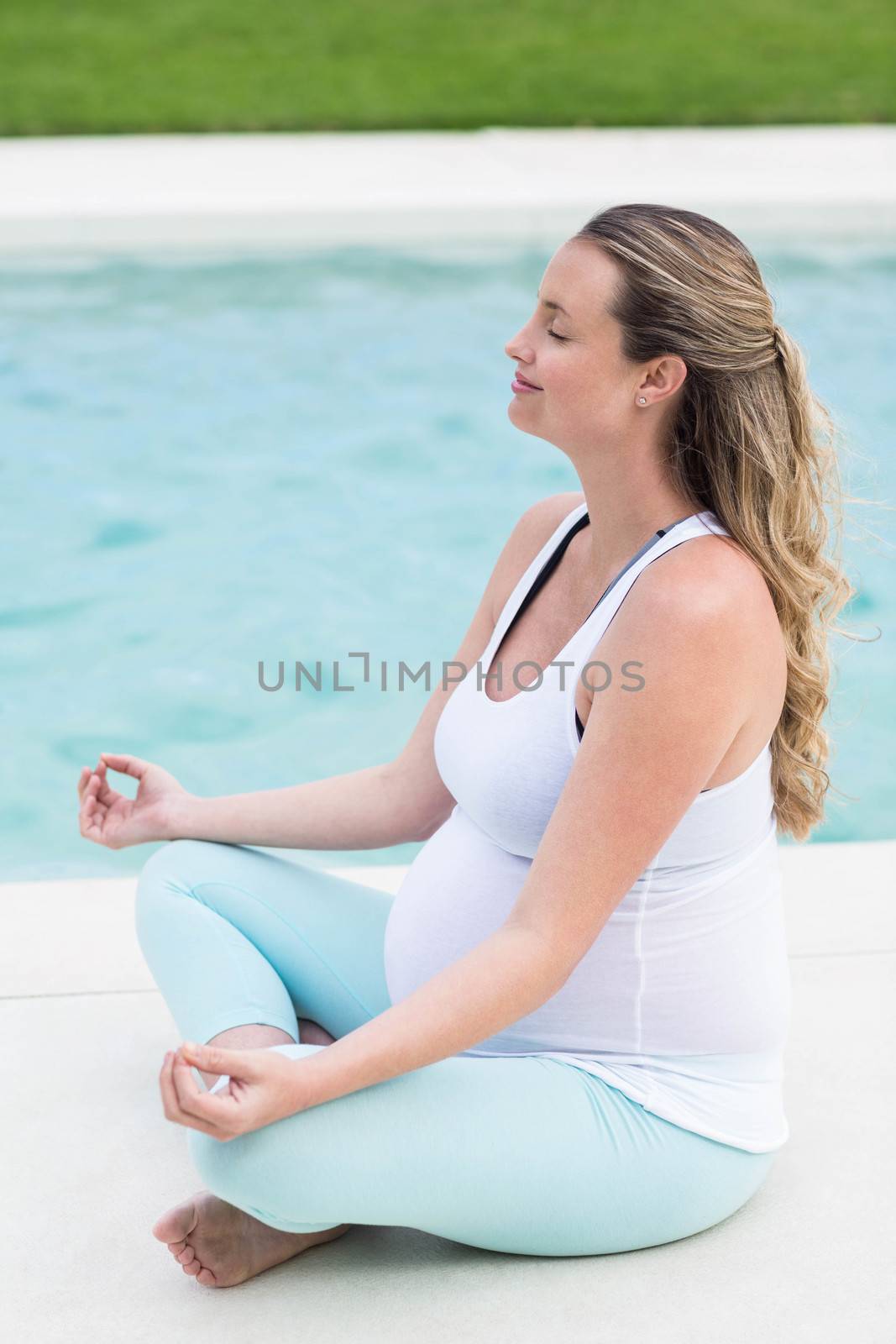 Pregnant woman doing yoga next to the swimming pool