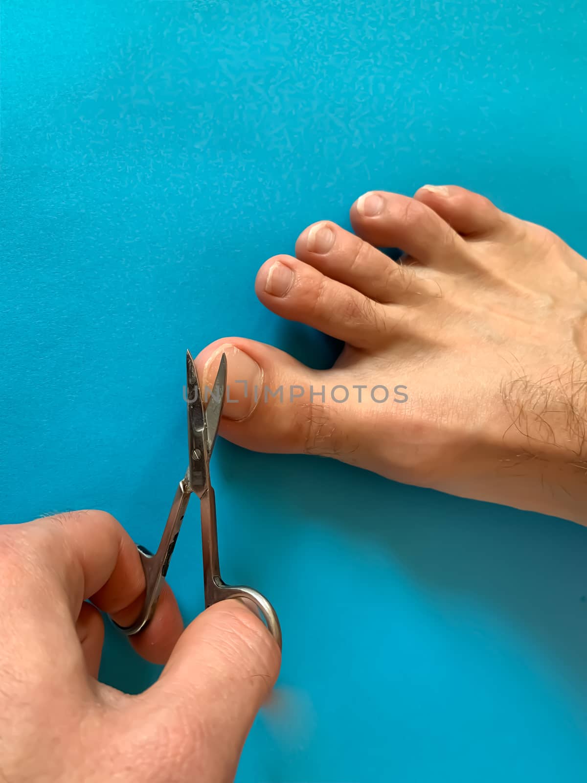 Male's hand holding on nail scissors, Man use nail scissors cutting their thumbs nail on foot toes on blue background