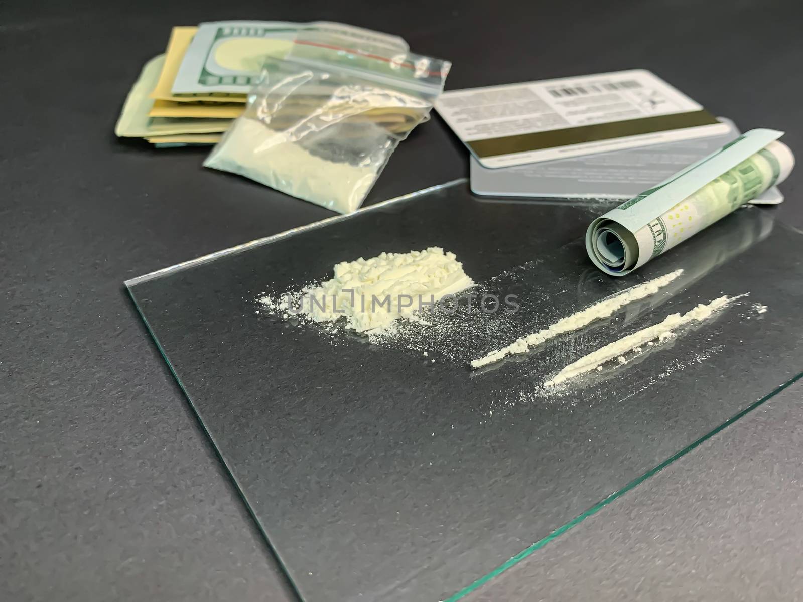 Rolled 100 us dollars, 2 lines of cocaine, plastic bag with illegal drugs and credit cards on a gray background. Drug addiction. Stock image.