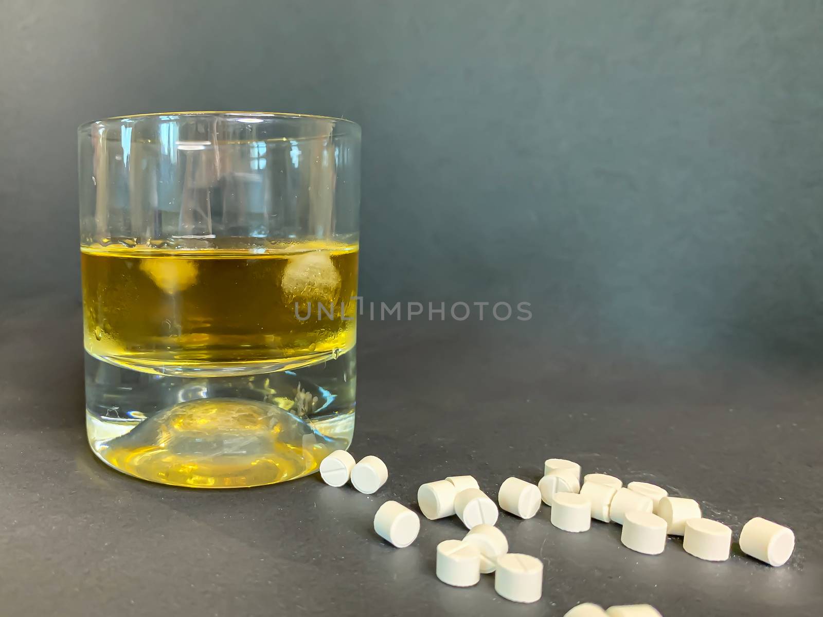 A glass of whiskey with ice and a lot of white pills on a gray background. Suicide concept with tablets and alcohol. Stock image.