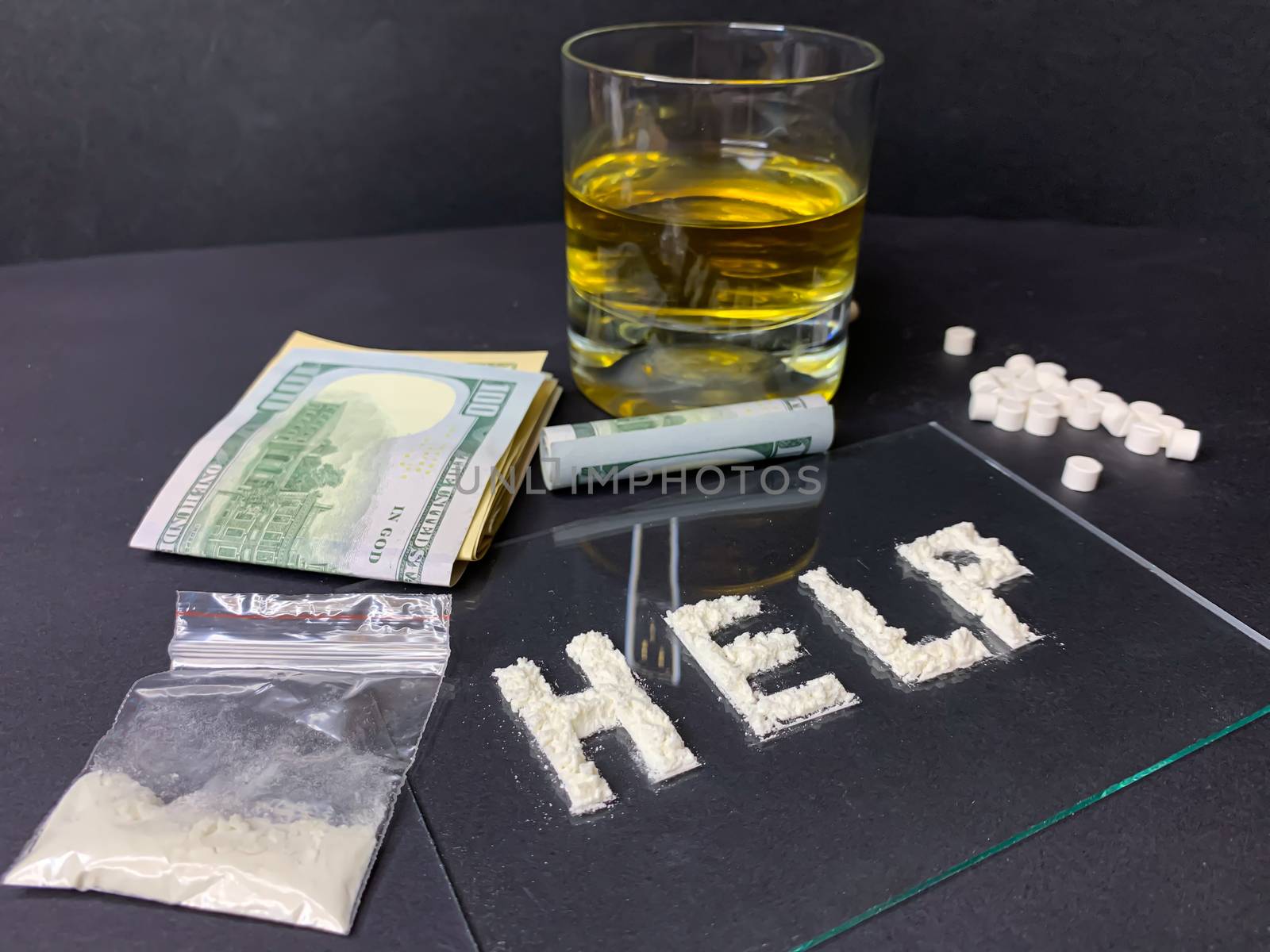 Pills; us dollar banknotes; whiskey and cocaine; on a gray background. Stop drugs concept. A word "help" written with cocaine. Stock image.