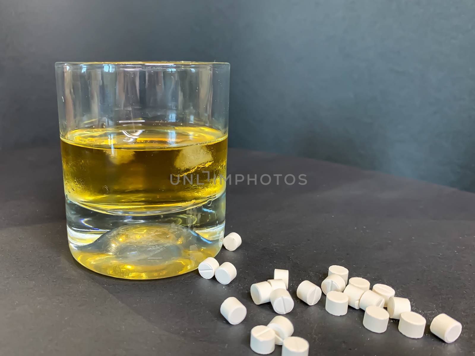 A glass of whiskey with ice and a lot of white pills on a gray background. Suicide concept with tablets and alcohol. Stock image.