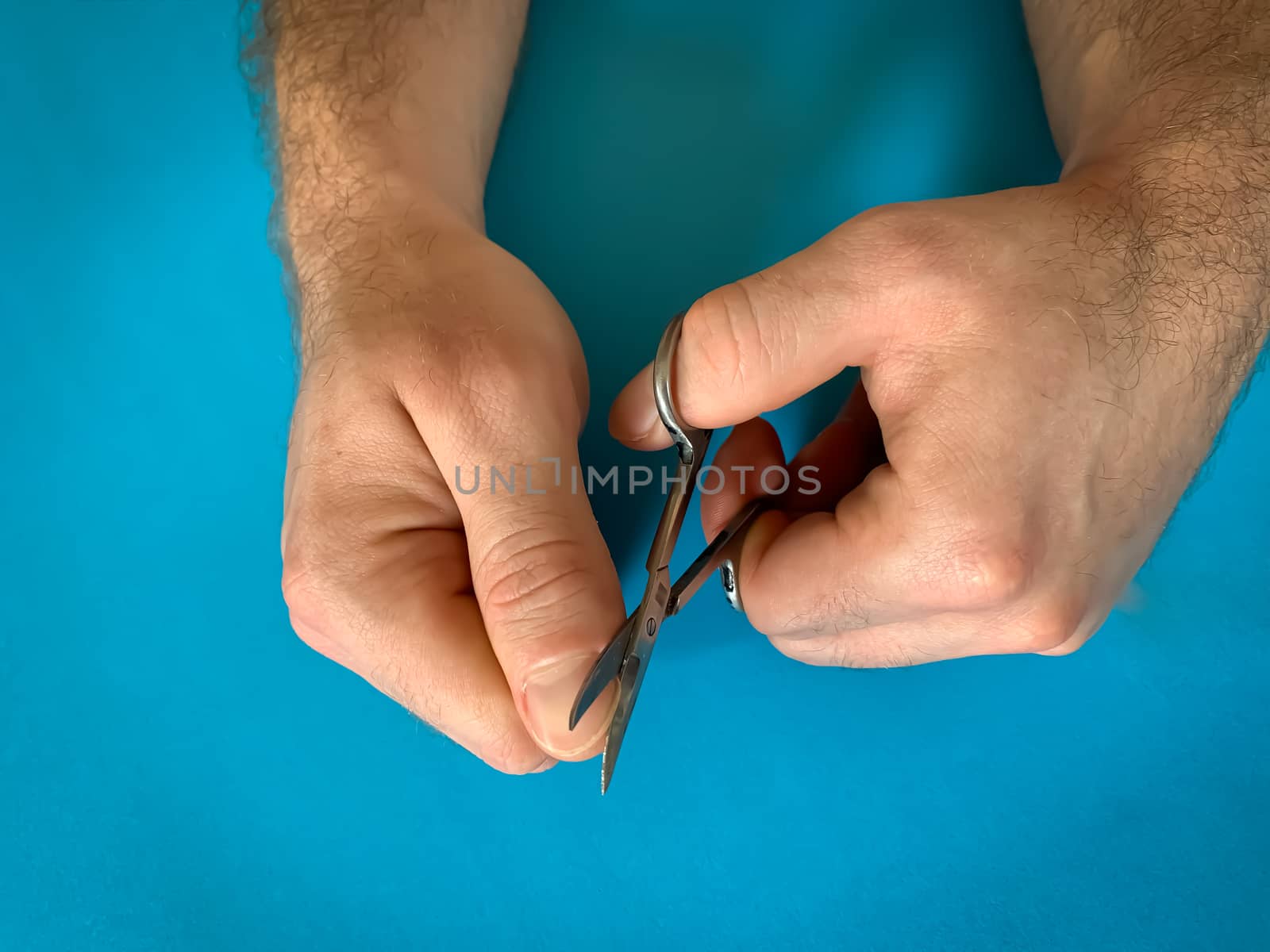 Male's hand holding on nail scissors, Man use nail scissors cutting their thumbs nail on blue background