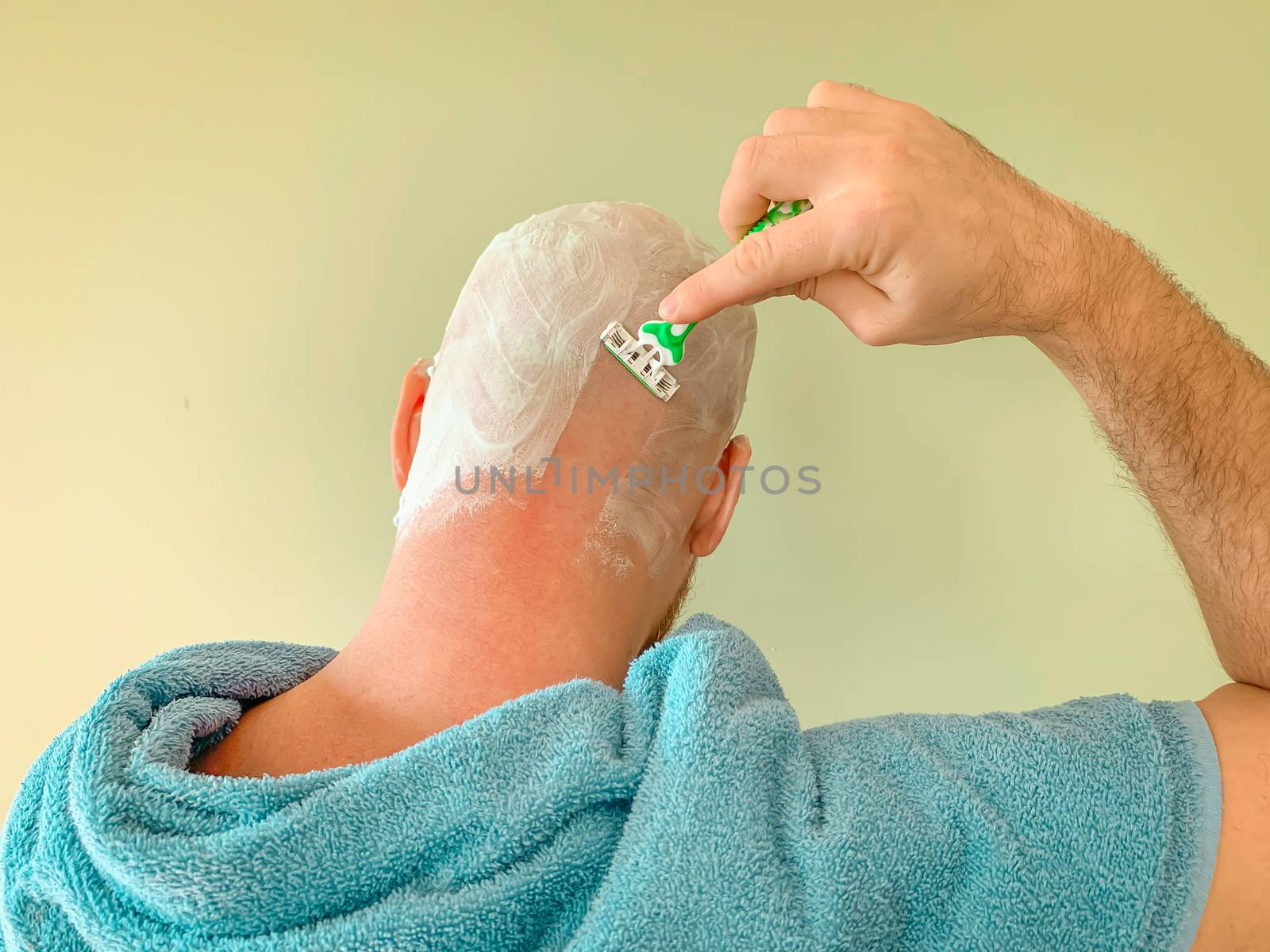 Young man shaving his head by himself, view from back