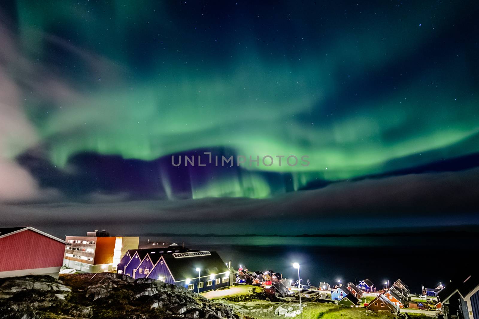 Green bright northern lights hidden by the clouds over the Inuit village at the fjord, Nuuk city, Greenland