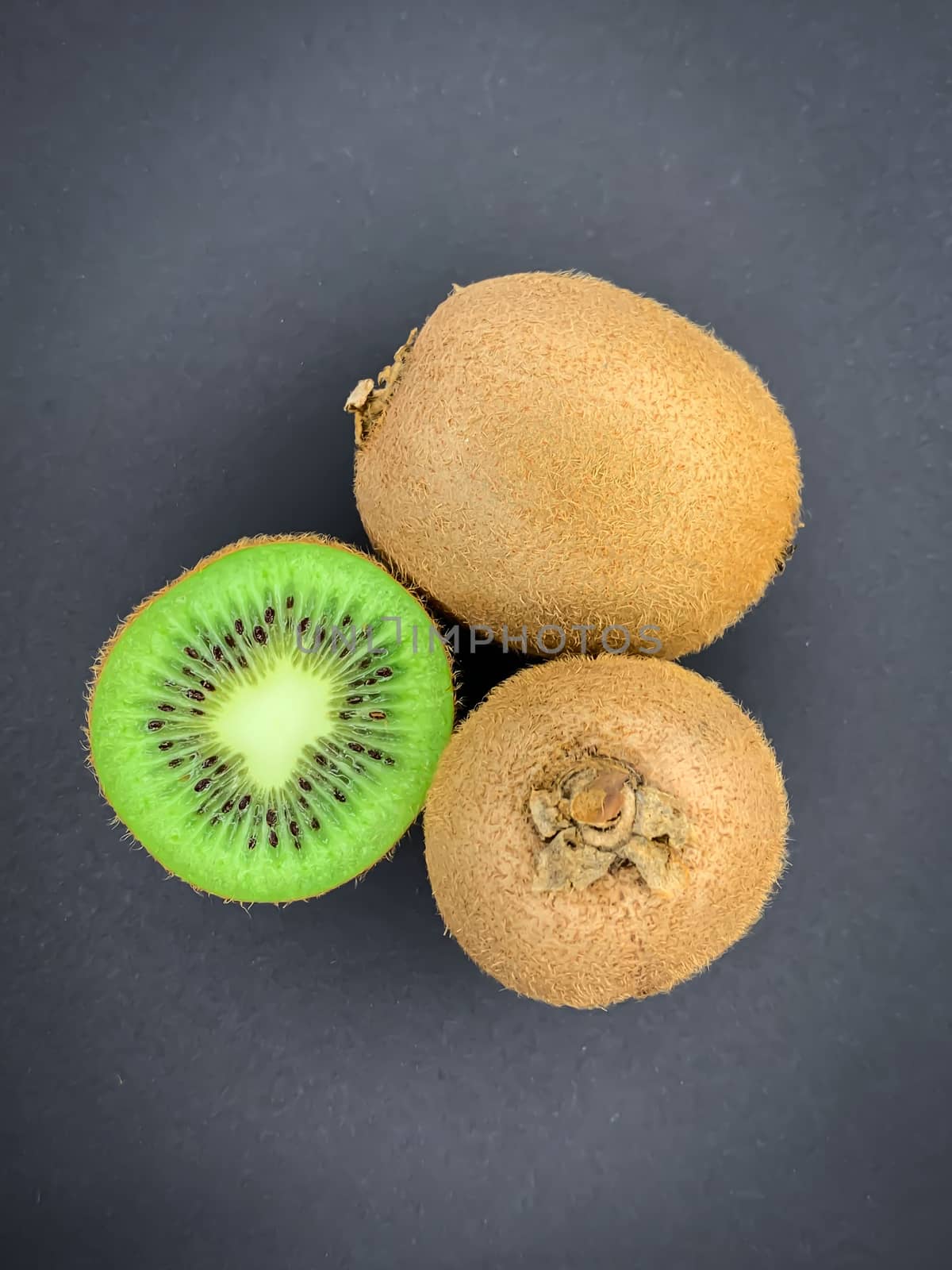 Fresh ripe whole and half kiwi fruit on a gray background. Vertical flat lay