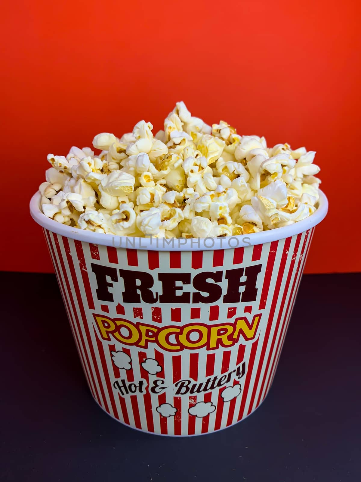 Close up delicious fresh buttery popcorn in a stripped red and white bowl on red background