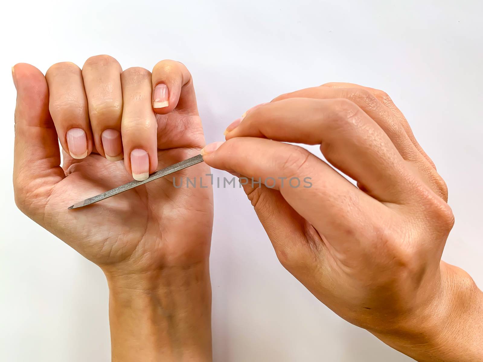 Woman's girl's hand filing nails with metal nail file on a white background. Self manicure at home