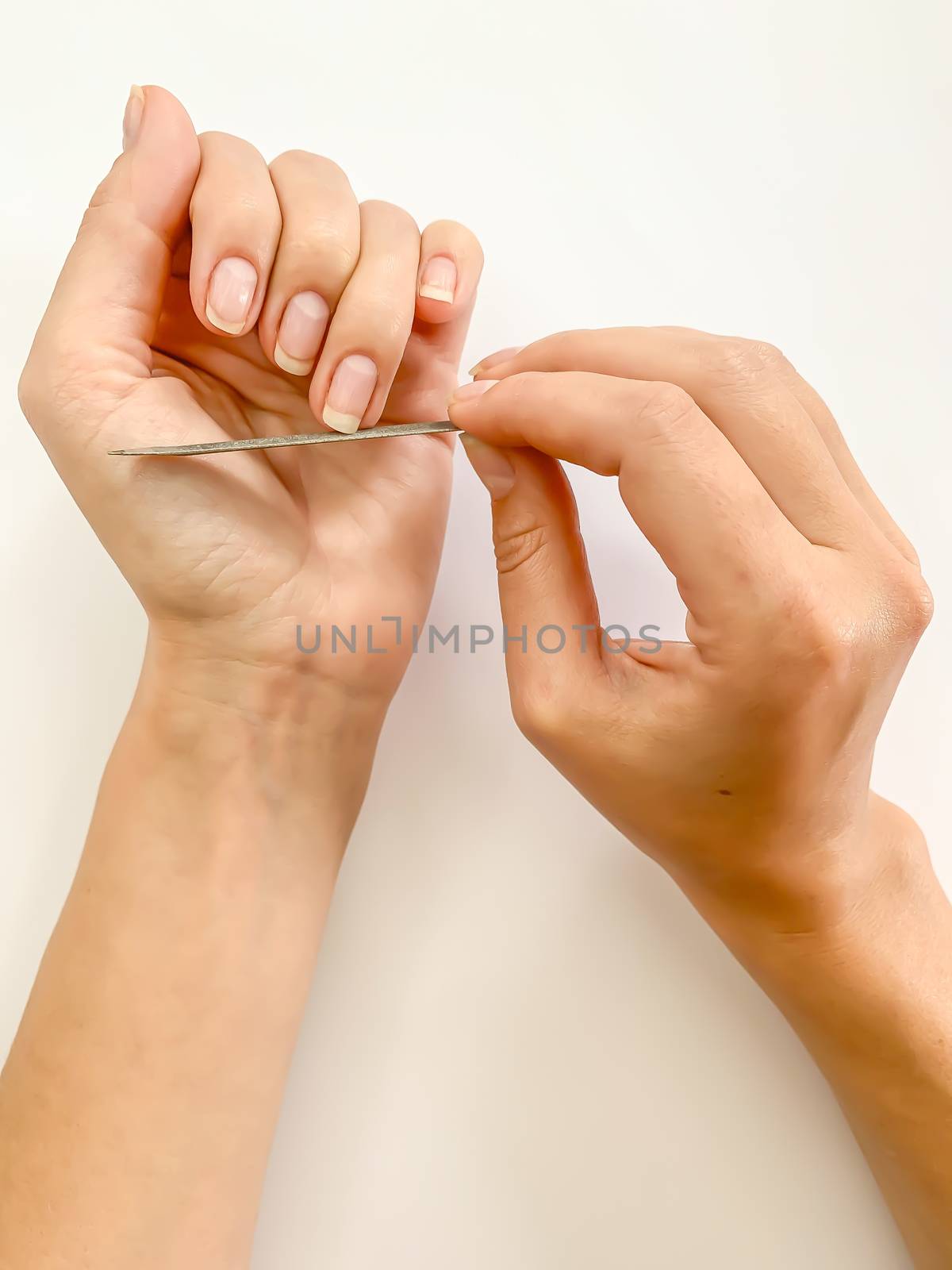 Woman's girl's hand filing nails with metal nail file on a white background. Self manicure at home