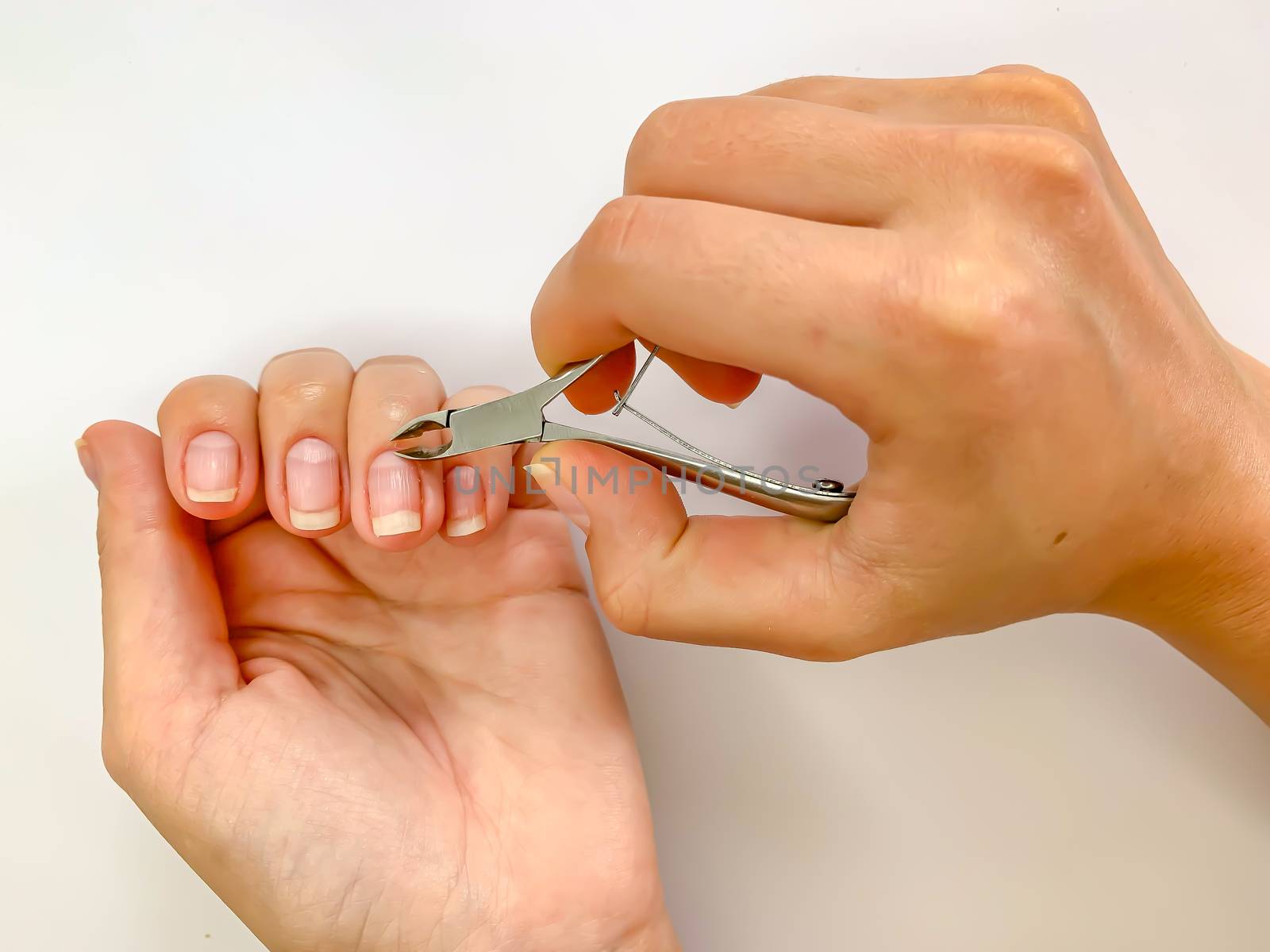 Close up of hands. Self manicure at home trimming cuticles on white background. Manicure and skin care. 