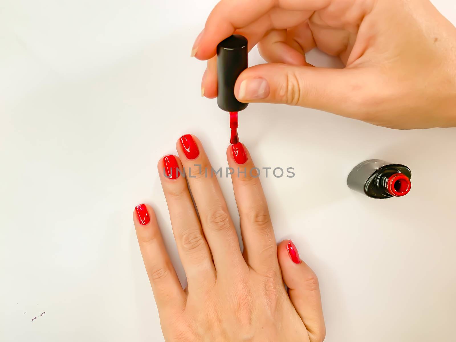 Close up female woman painting her nails with nail polish in red color on a white background. Self manicure at home