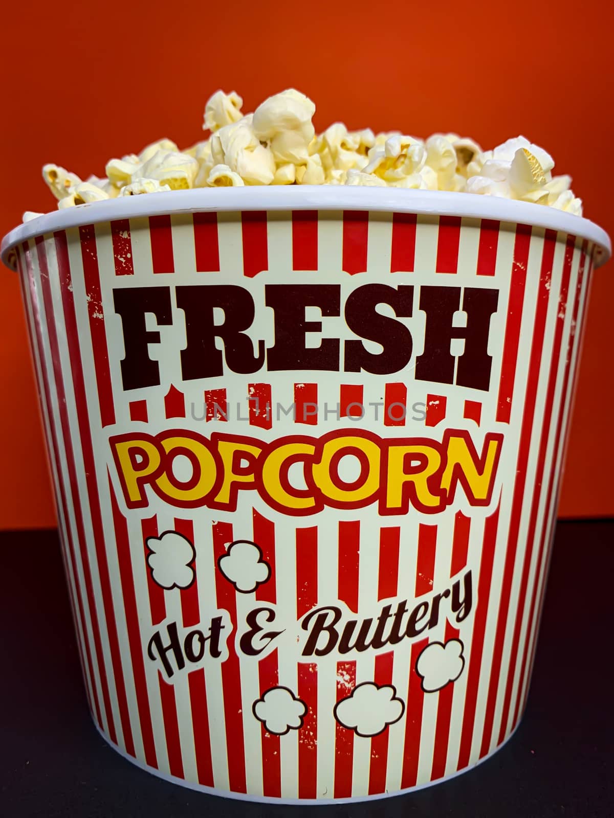 Close up delicious fresh buttery popcorn in a stripped red and white bowl on red background