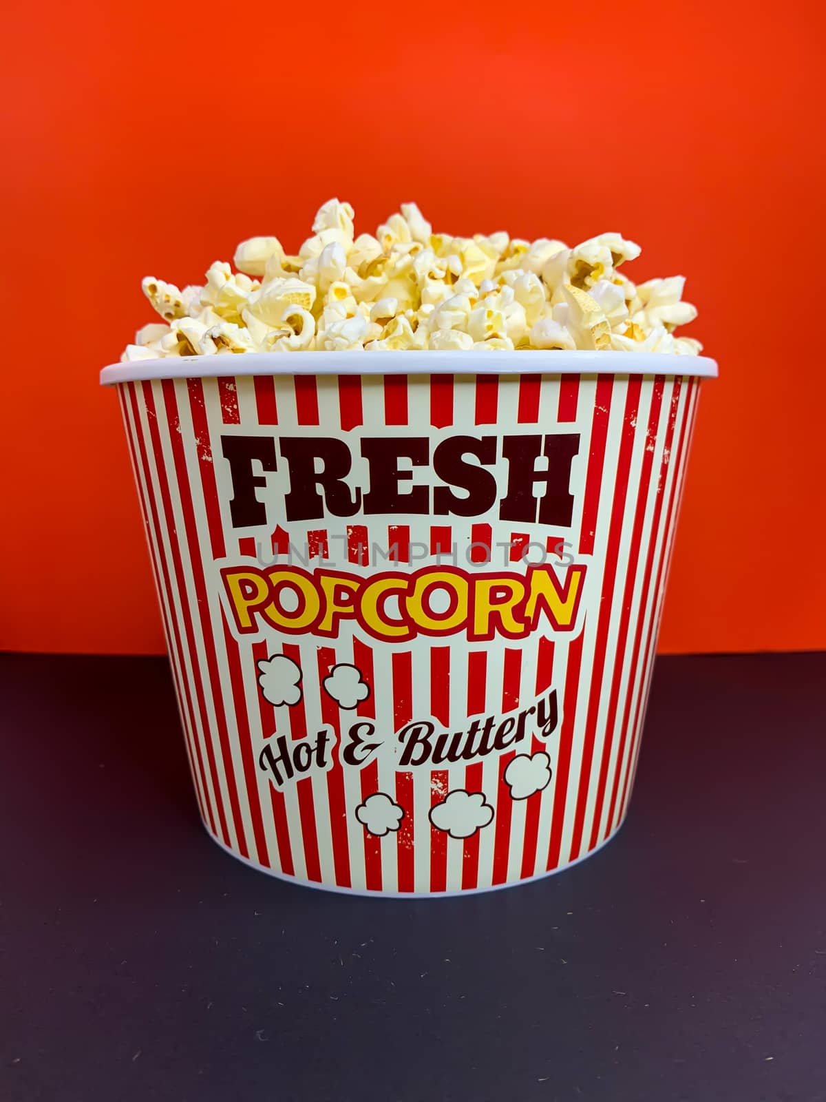 Close up delicious fresh buttery popcorn in a stripped red and white bowl on red background