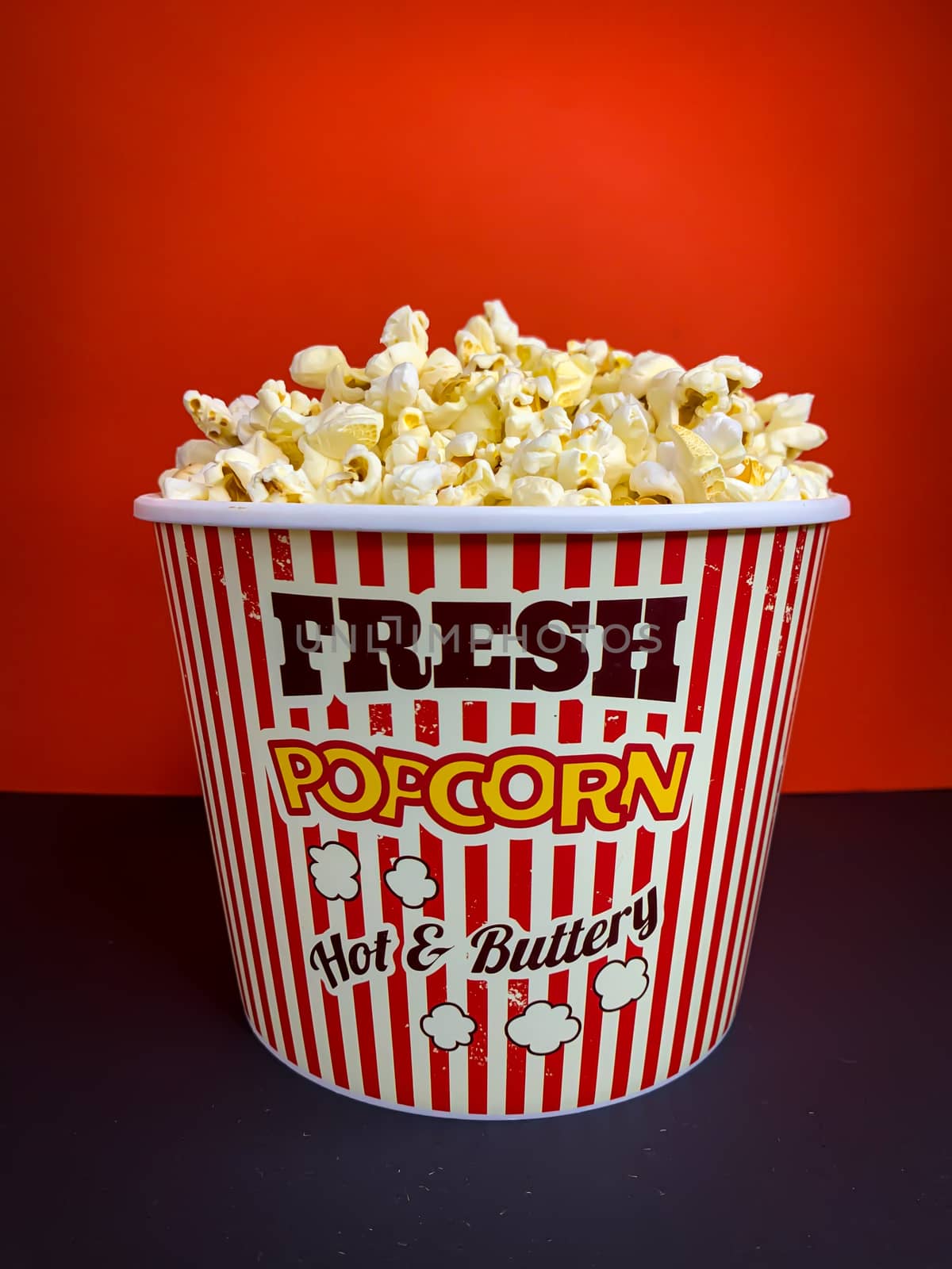 Close up delicious fresh buttery popcorn in a stripped red and white bowl on red background