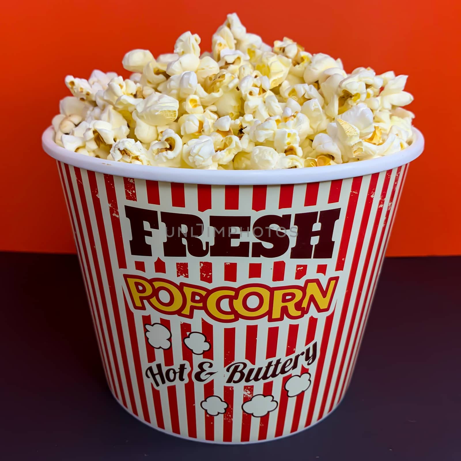 Close up delicious fresh buttery popcorn in a stripped red and white bowl on red background