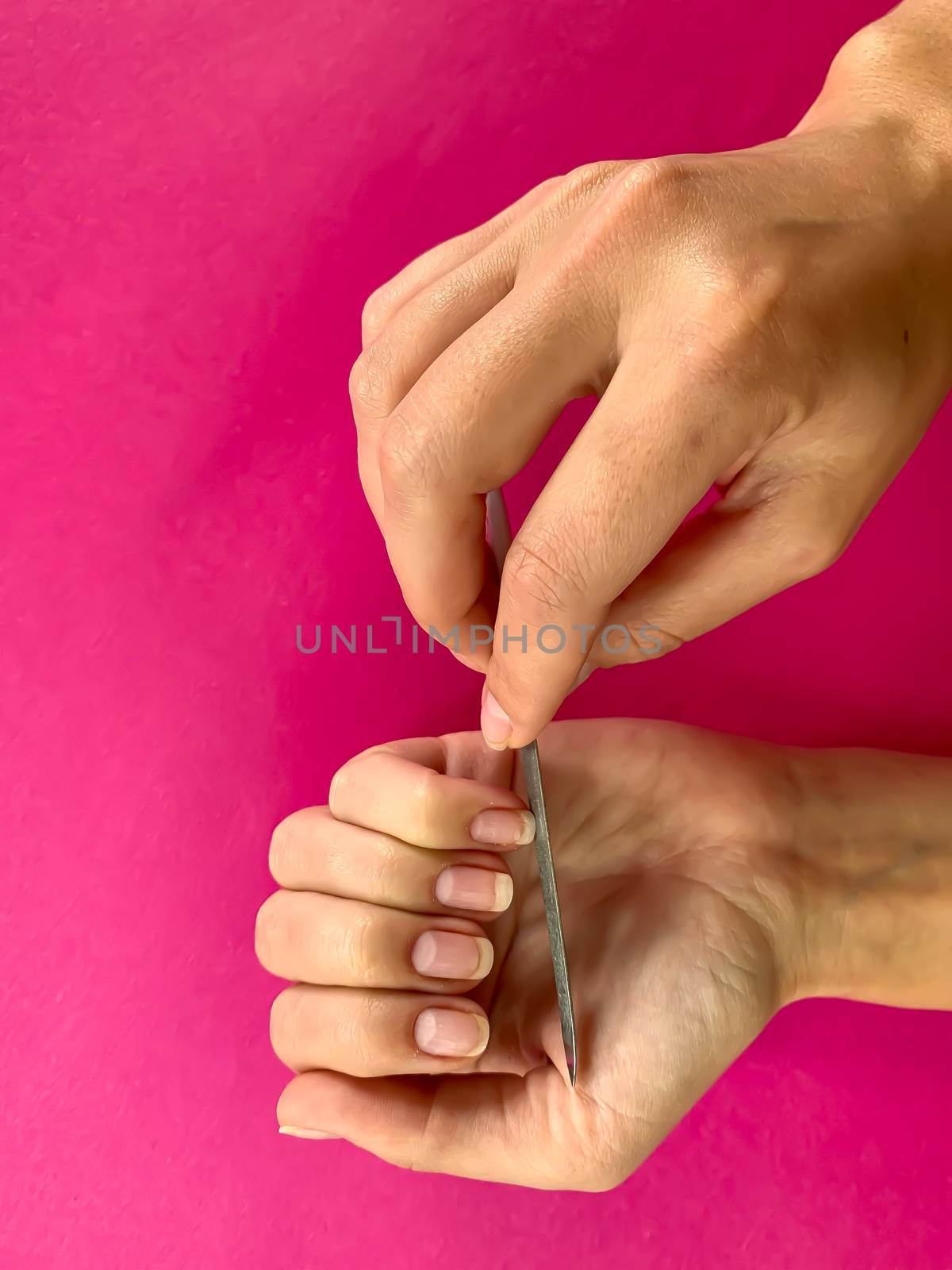 Woman's girl's hand filing nails with metal nail file on a pink background. Self manicure at home