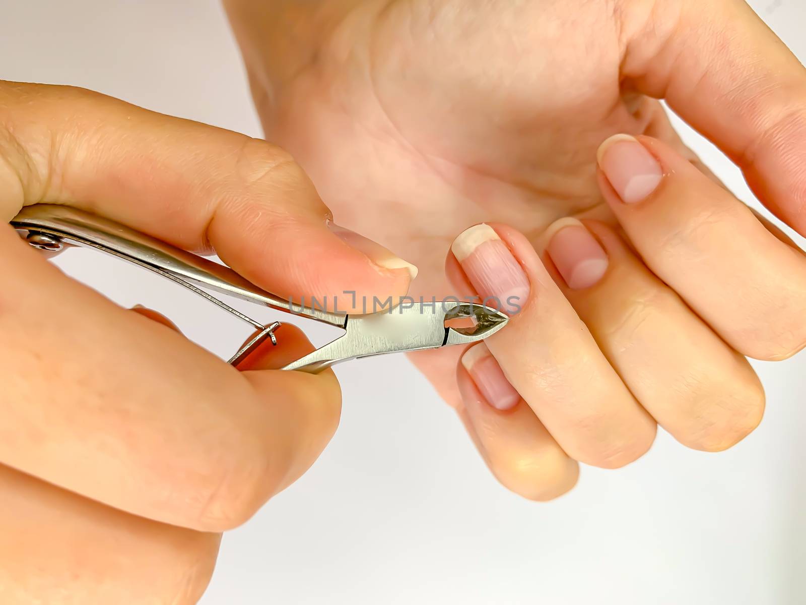 Close up of hands. Self manicure at home trimming cuticles on white background. Manicure and skin care. 