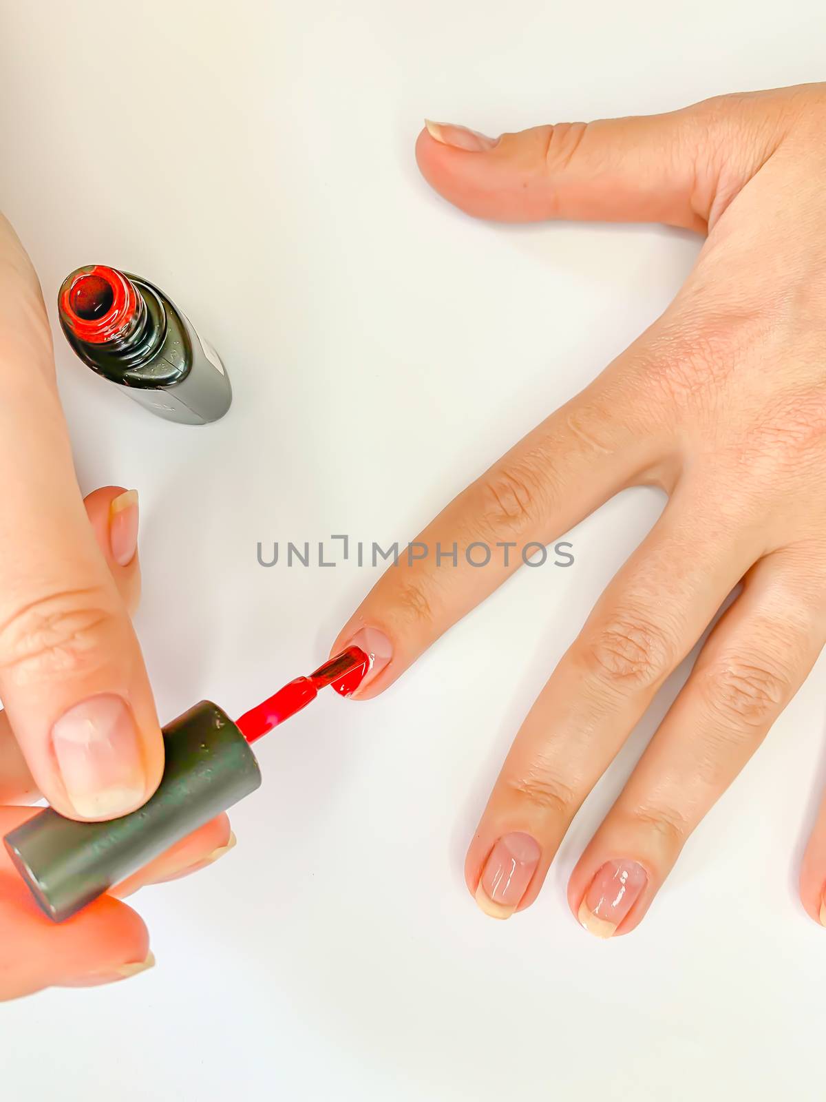 Close up female woman painting her nails with nail polish in red color on a white background. Self manicure at home