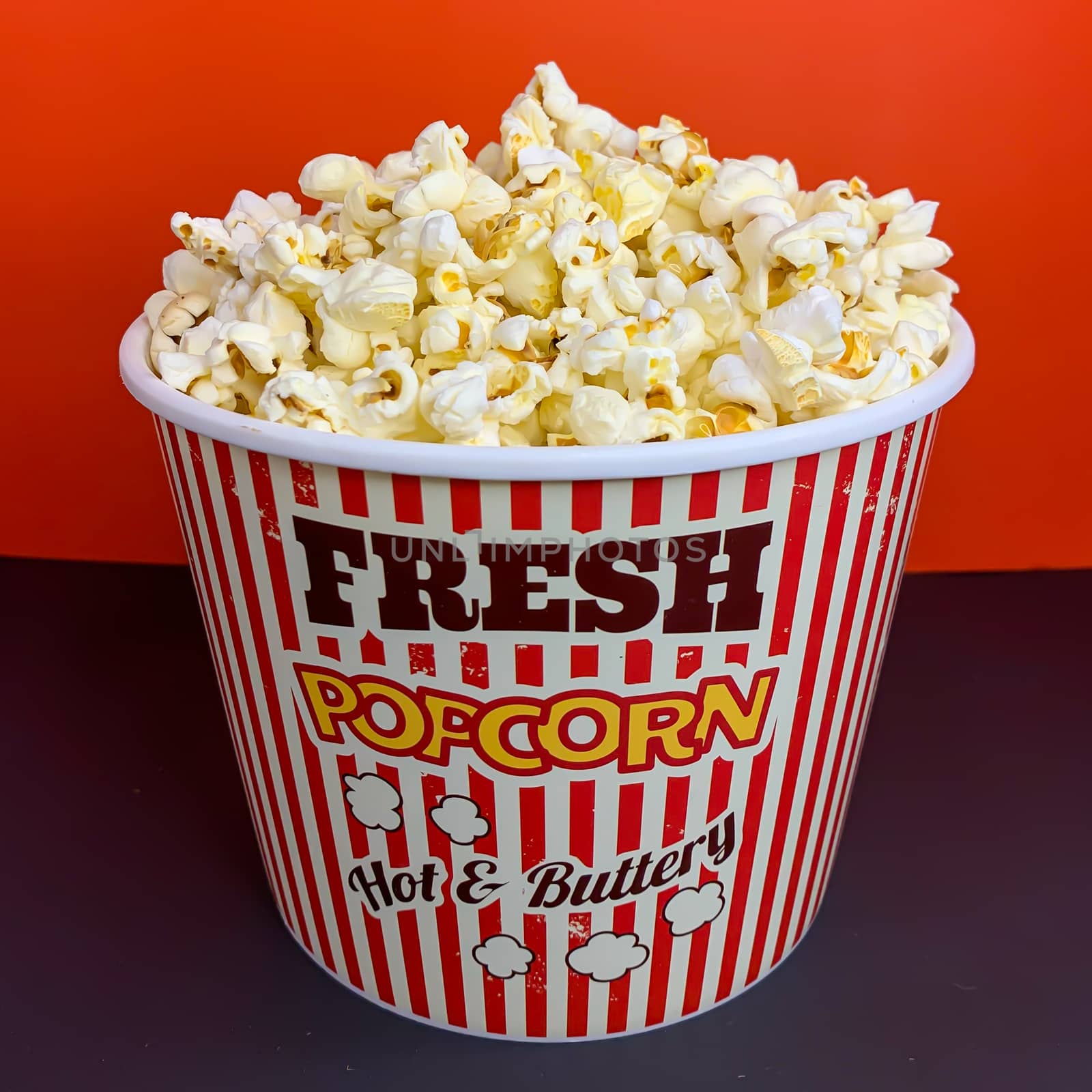 Close up delicious fresh buttery popcorn in a stripped red and white bowl on red background