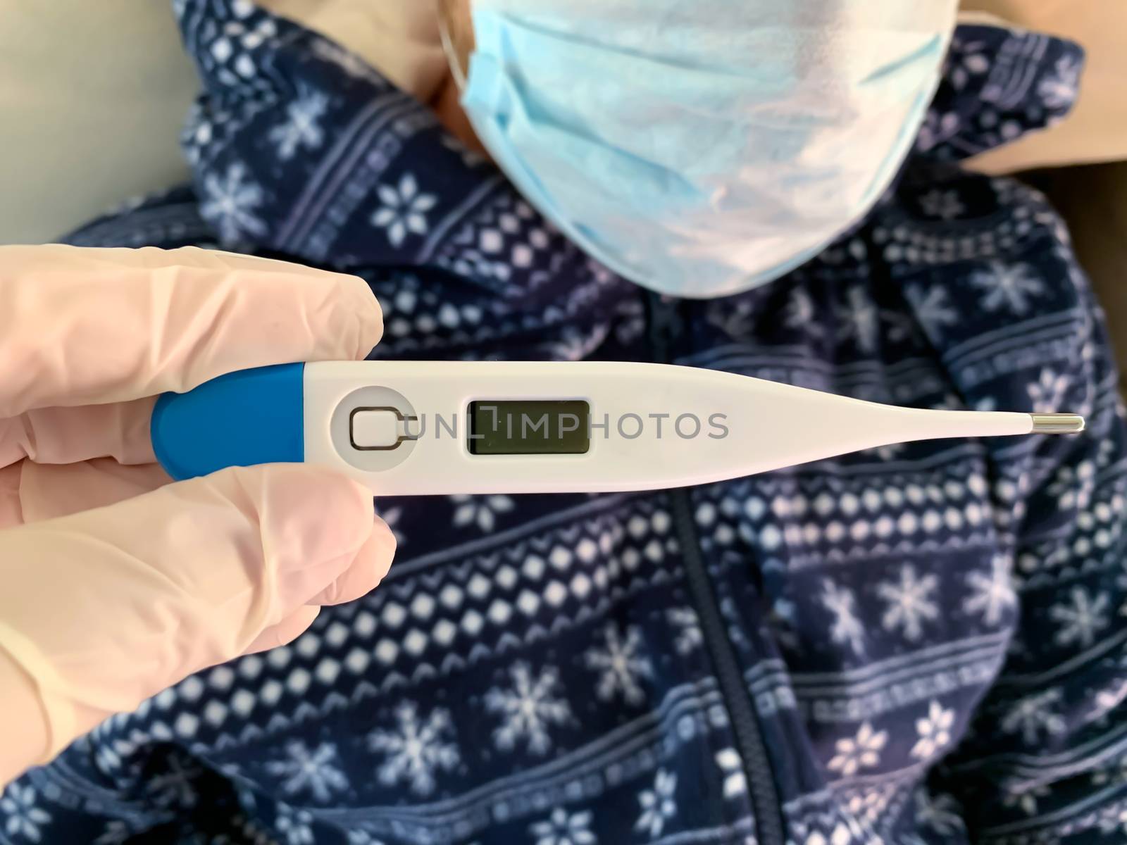 Hand in medical glove holds a digital thermometer. Sick male man patient in blue with medical face mask on a background