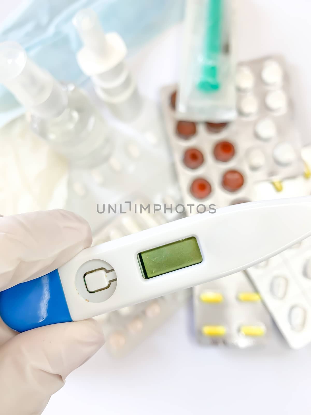 Digital thermometer for measuring body temperature in hand in glove of a woman on white background with many pills and medicines. Vertical image
