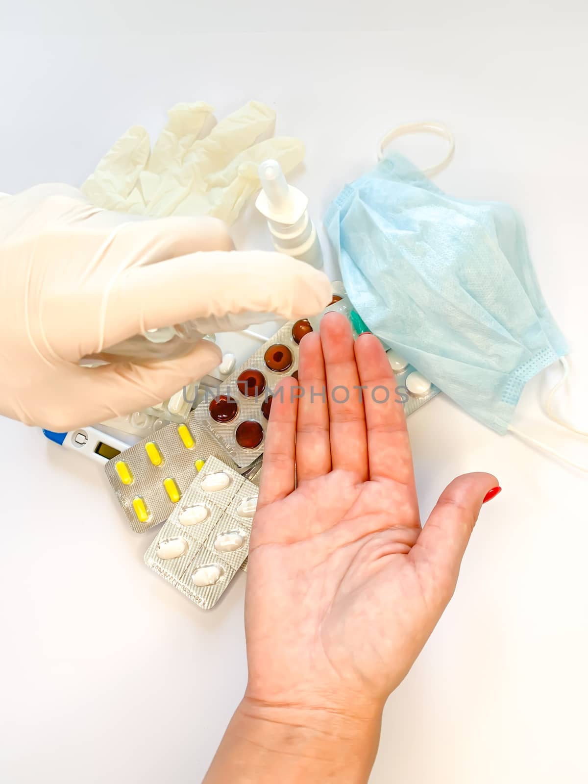 Hand of female in medical glove that applying alcohol spray or anti bacteria spray to prevent spread of germs, bacteria and virus on white background with medical tools and pills. Personal hygiene