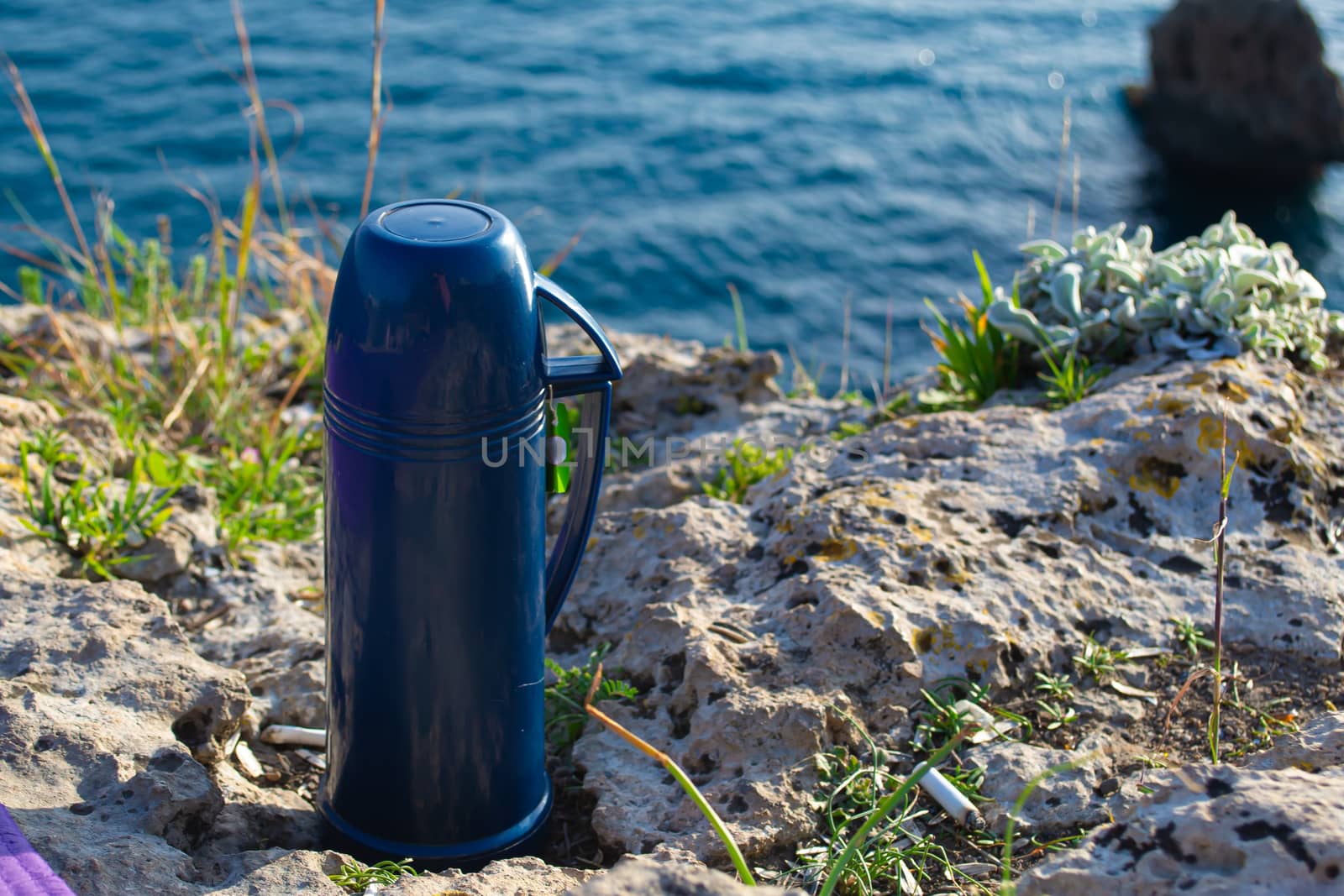 Blue thermos with tea picnic by the seaside on sunny day