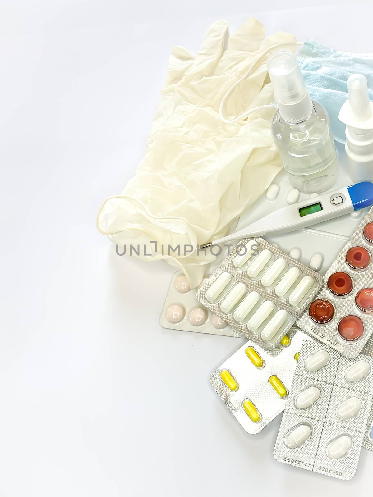 Different medicines: tablets, pills in blister pack, medications drugs, medical gloves, mask, syringe, thermometer, spray, sanitizer on a white background. Vertical photo with space for text