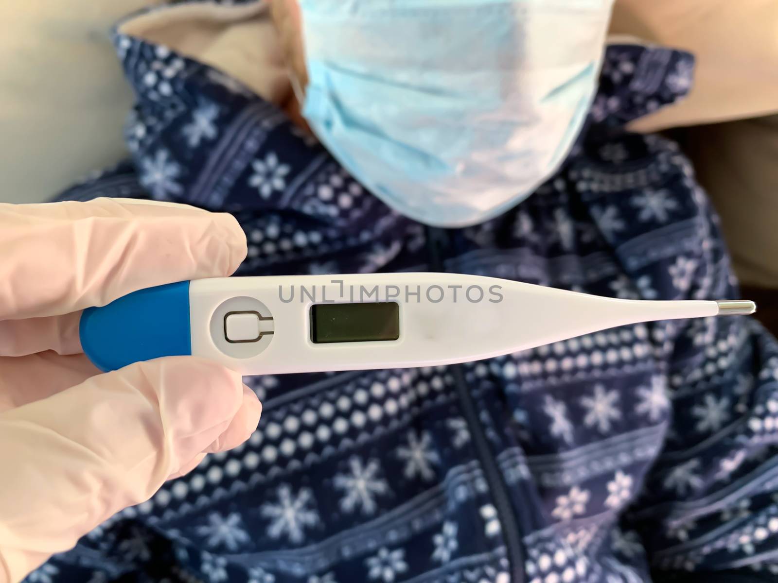 Hand in medical glove holds a digital thermometer. Sick male man patient in blue with medical face mask on a background