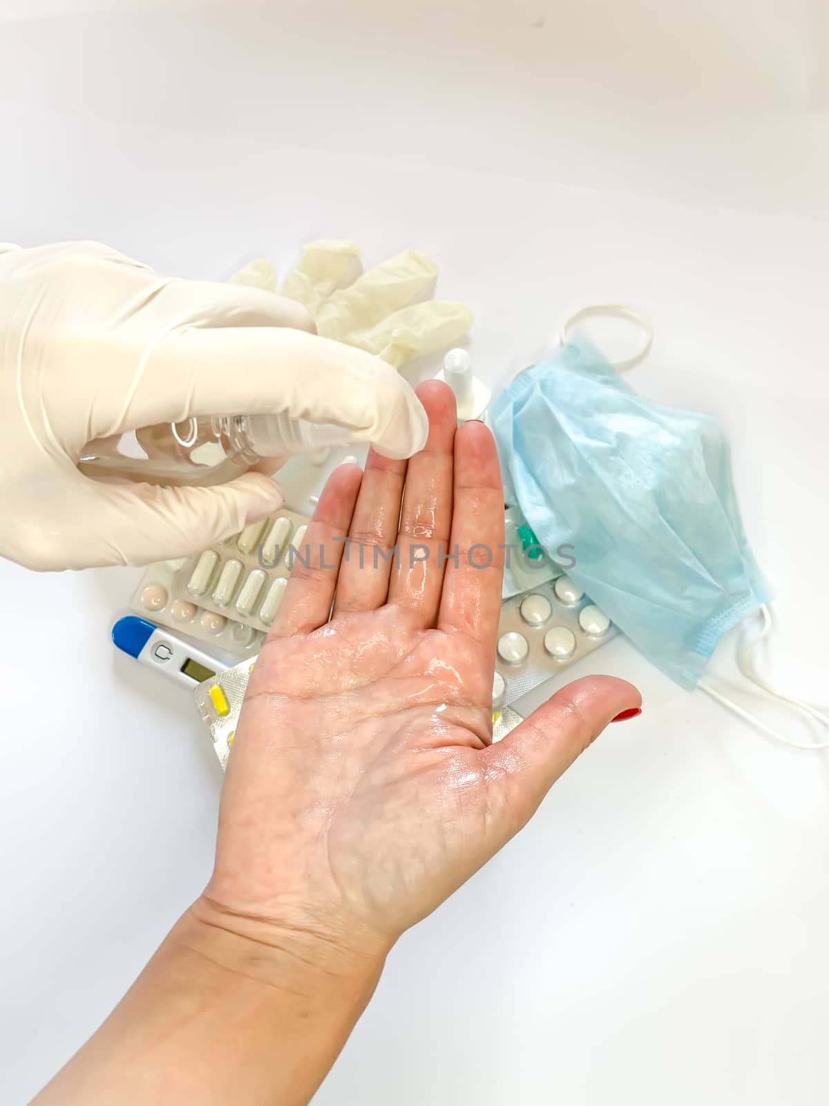 Hand of female in medical glove that applying alcohol spray or anti bacteria spray to prevent spread of germs, bacteria and virus on white background with medical tools and pills. Personal hygiene
