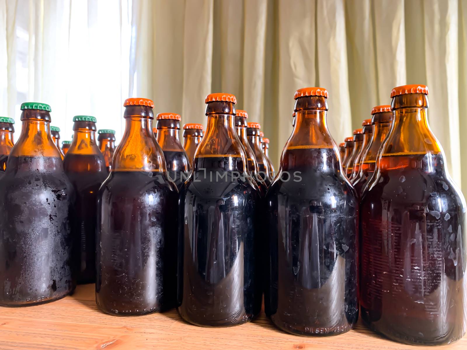Home made fresh craft beer bottles on a wooden table. Close up rows of beer bottles with orange caps horizontal image. Self made beer brewery at home