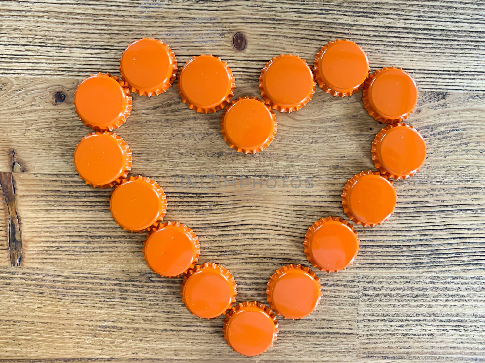 An orange love heart made from beer bottle tops lids on a rustic wooden table. Beer drinkers Valentine's day concept top view with empty space for text horizontal image