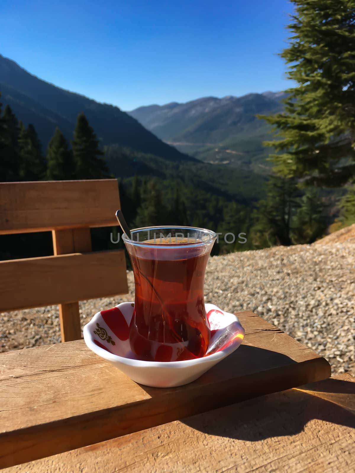 Tulip shaped cup of Turkish tea on wooden table with mountains and blue sky view