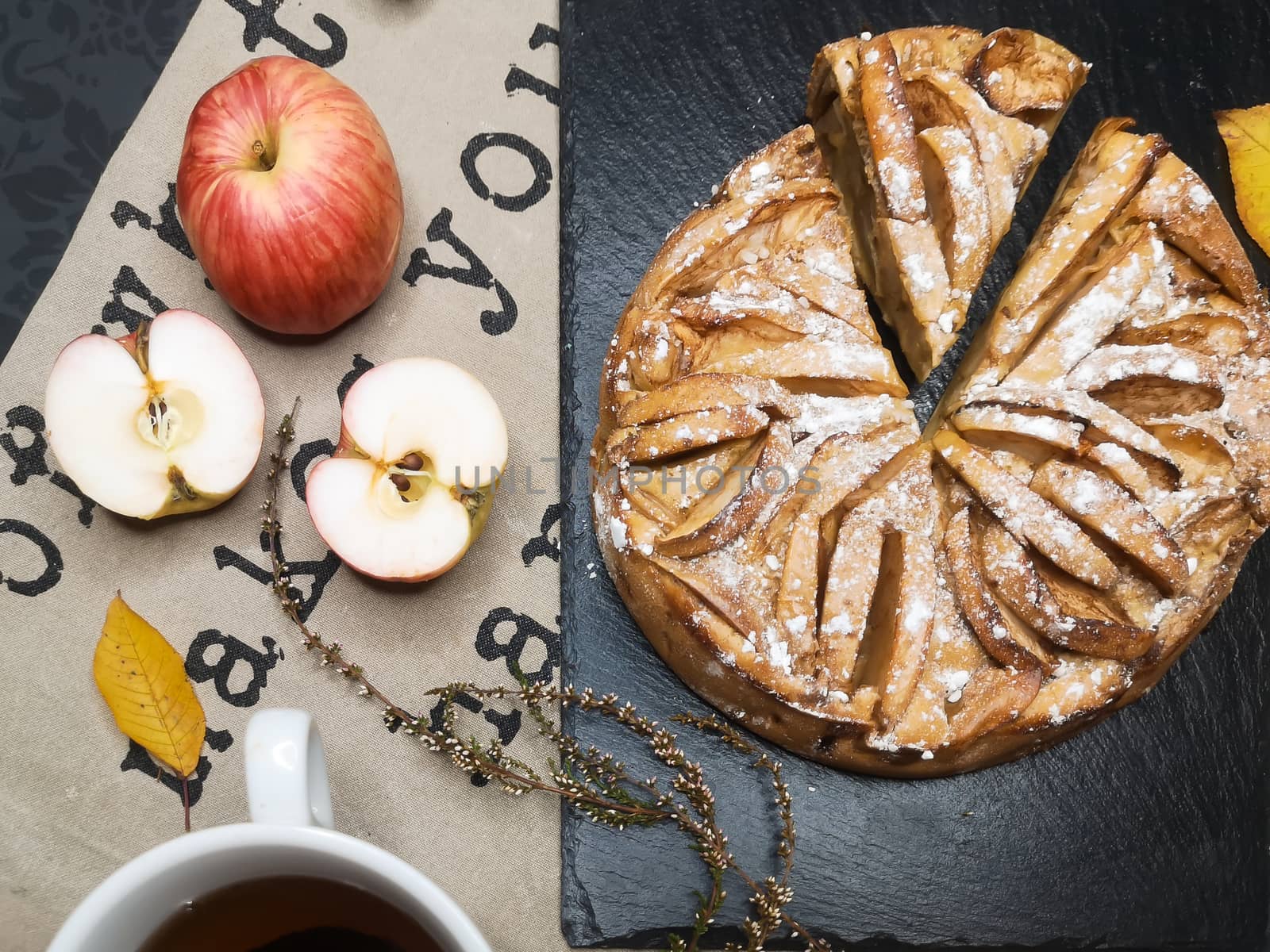 Homemade organic apple pie dessert with apples around it and a cup of tea flat view