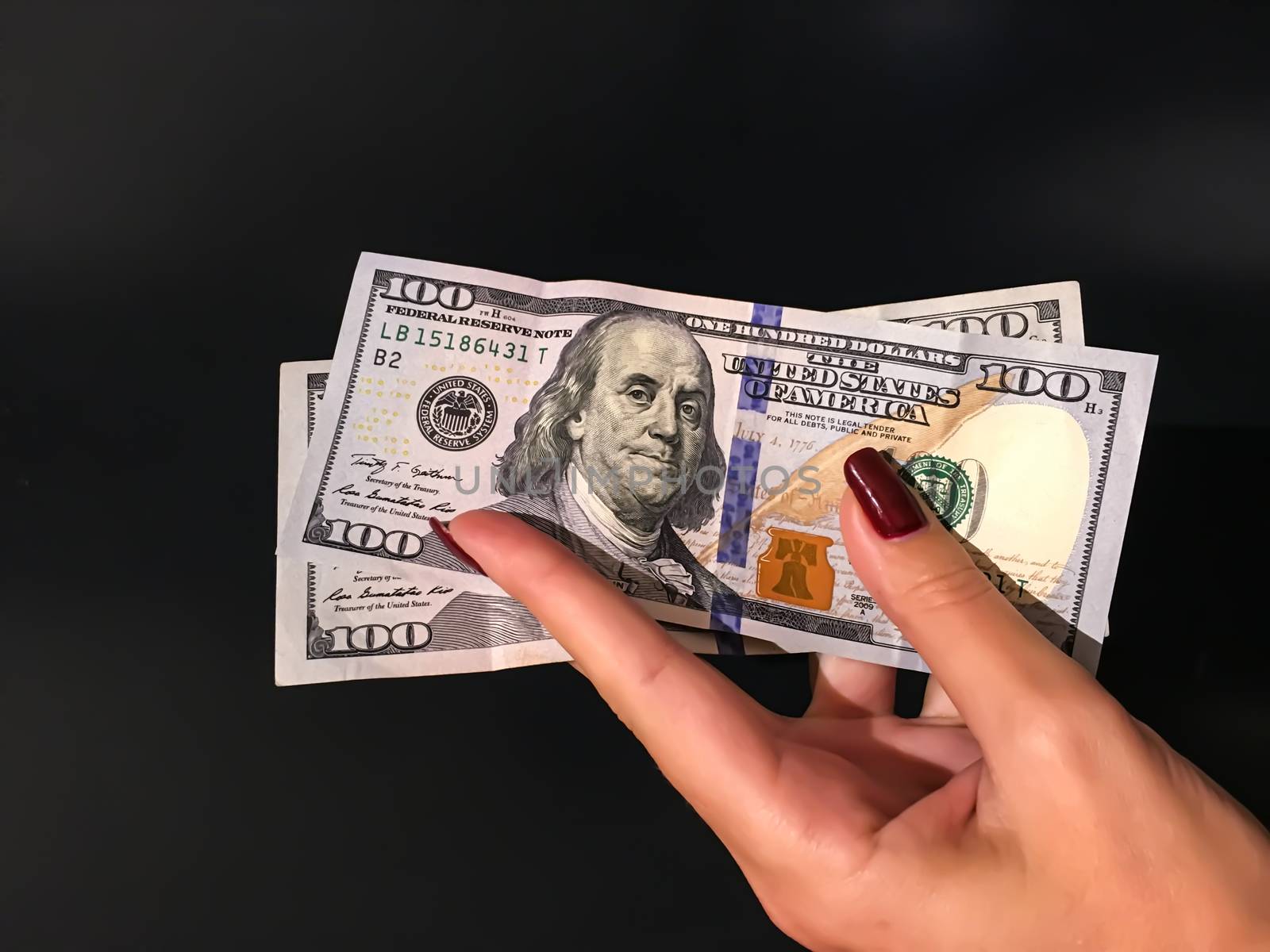 A Woman's Hand Holding two 100 Dollar Bills Banknotes on a grey  by AlonaGryadovaya
