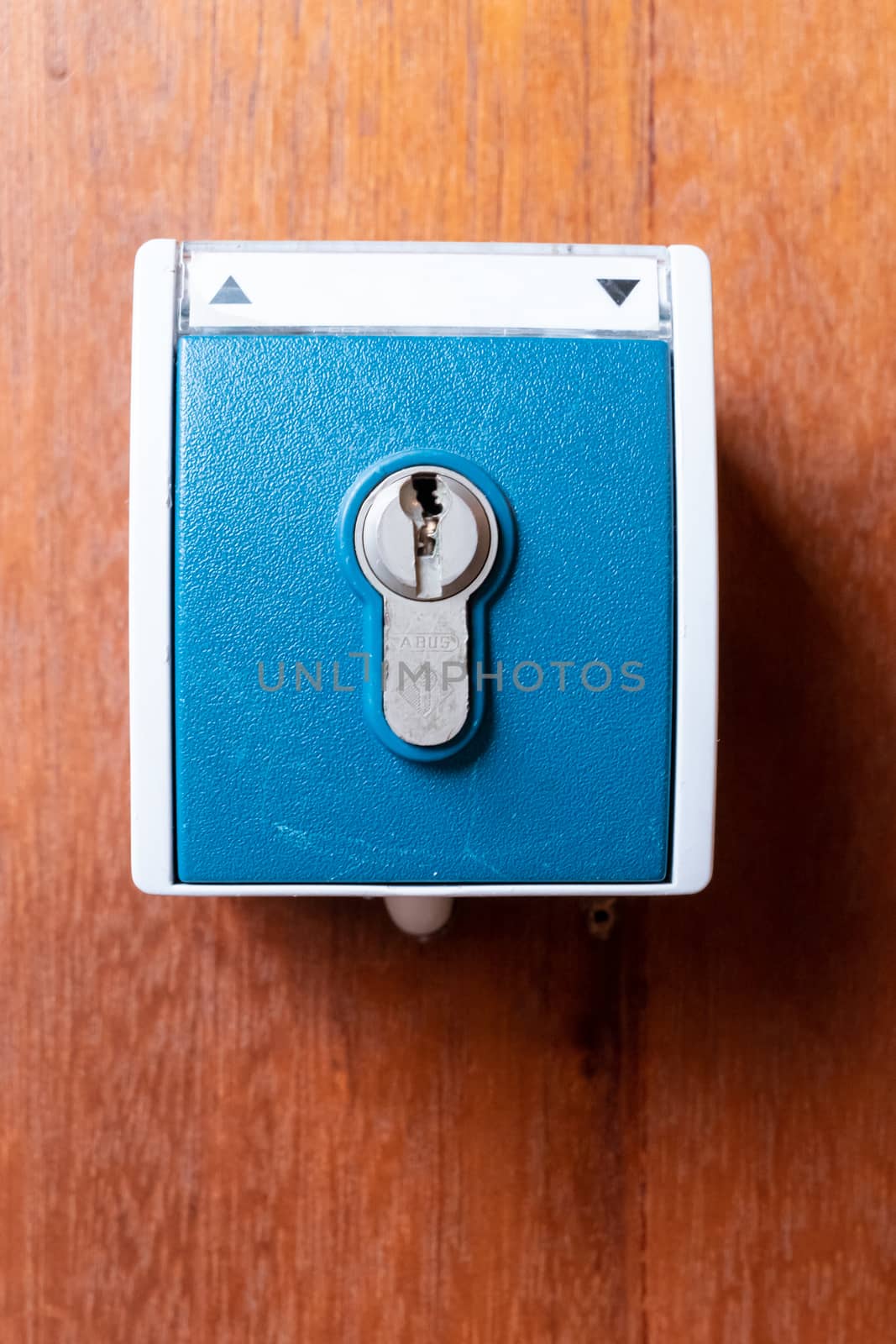 A blue key switch with cylinder screwed to a wooden wall with the symbols up and down to operate a switching operation with a key.