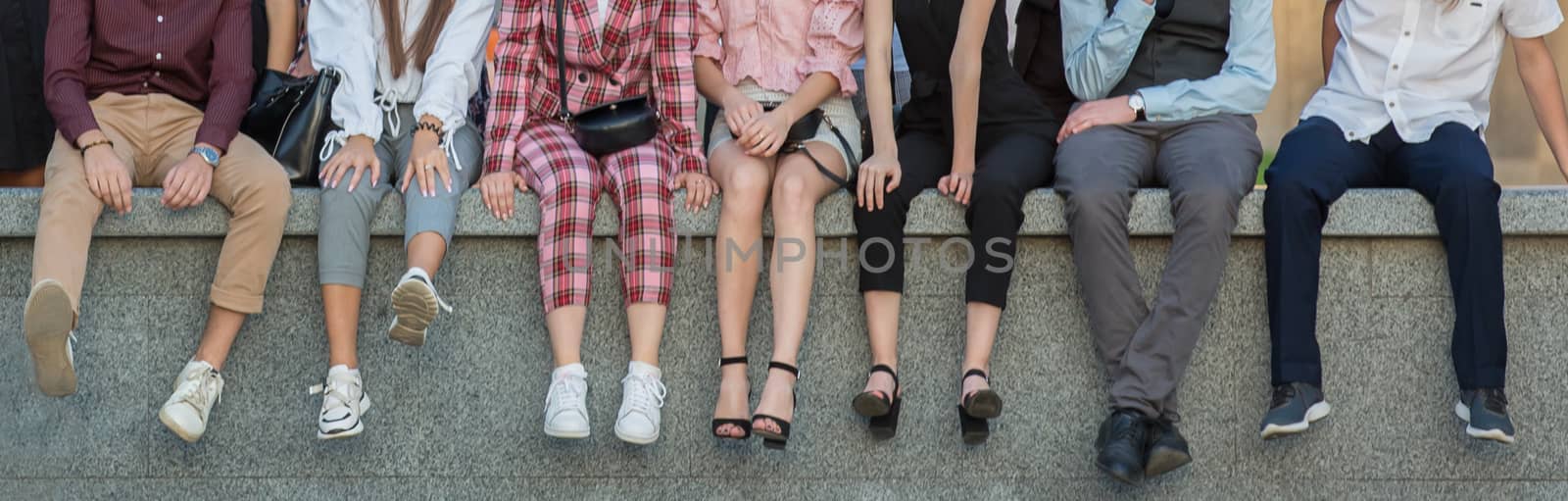 People are sitting in a row. A row of legs of seated students. Panoramic photo. Conceptual photo means friendship. Young people sit next to each other without visible faces.