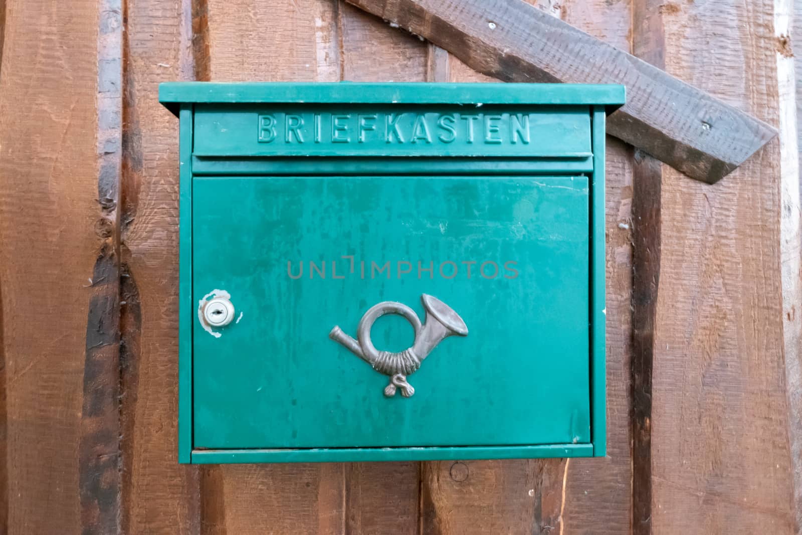 Krausnick, Brandenburg/Germany - 11.01.2020: A green mailbox with a post horn on the front, which is attached to a wooden wall and looks already used.