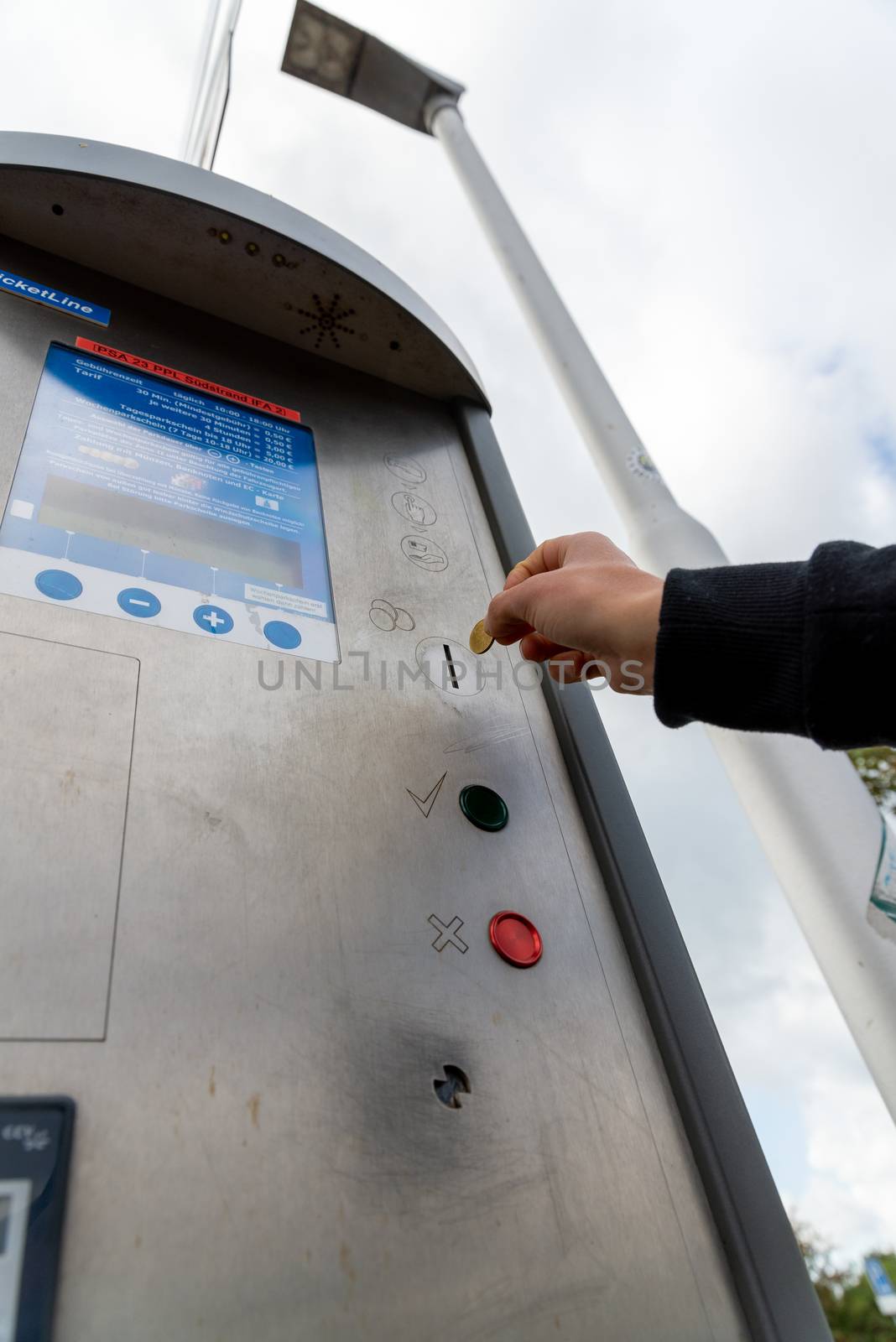 Hand with a coin in front of a parking ticket machine by Guinness