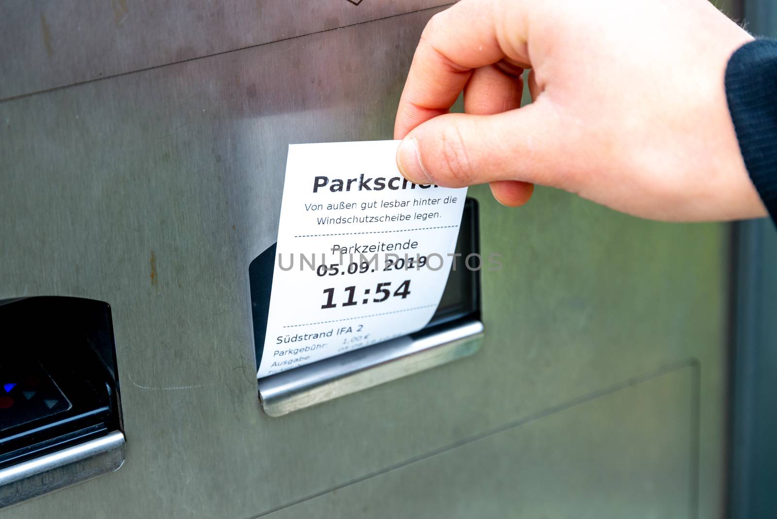 Fehmarn, Schleswig-Holstein/Germany - 05.09.2019: A hand pulls a parking ticket out of a parking ticket machine, on which it is noted when the parking time ends and where you can park. The machine is made of metal.