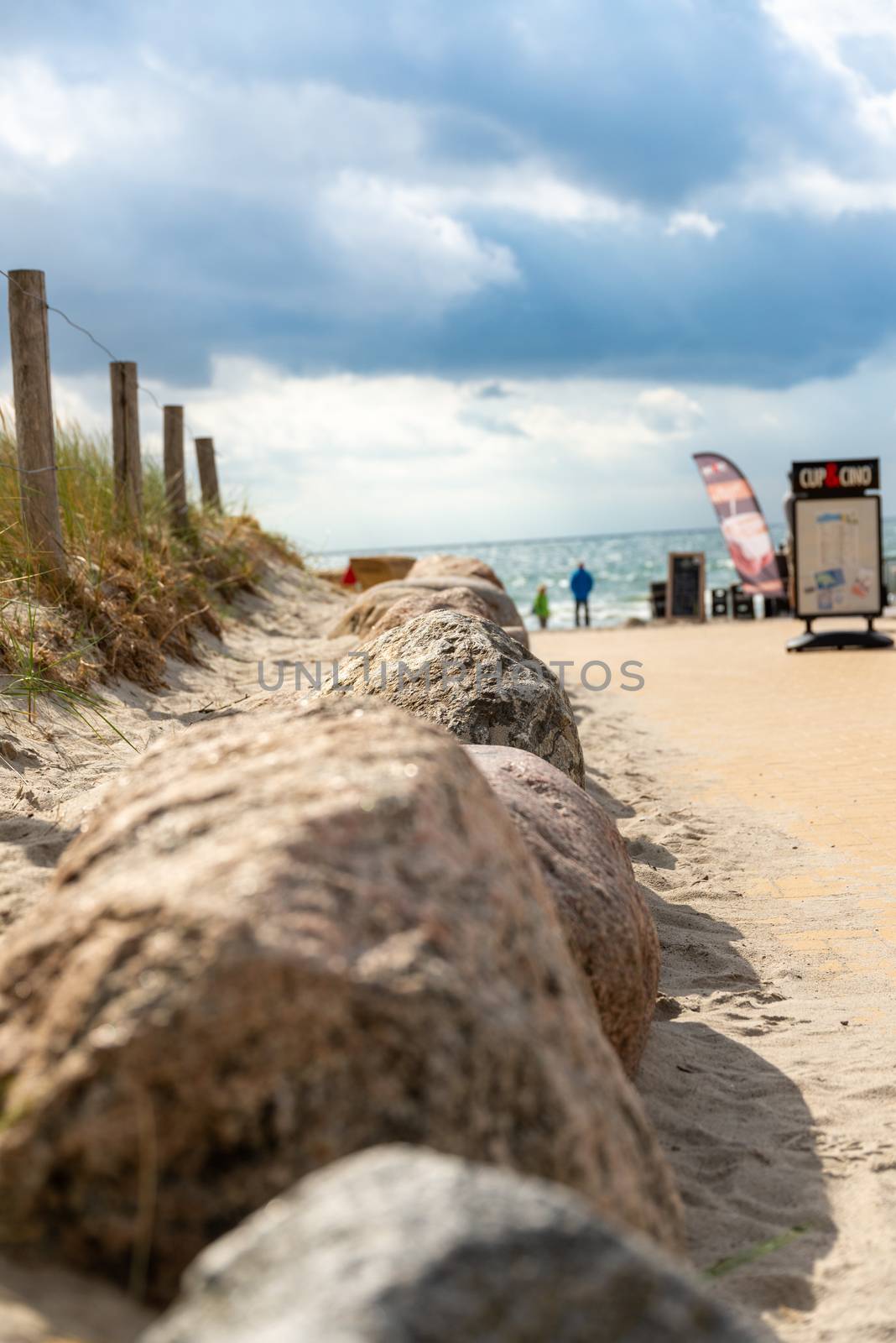 Fehmarn, Schleswig-Holstein/Germany - 05.09.2019: A path over a dune to the beach with tourist facilities in the background and as path border stones and a fence at the Baltic Sea island Fehmarn.