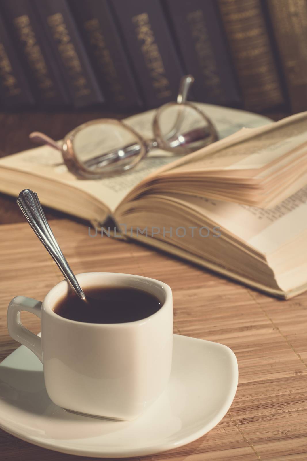 An open book and a cup of coffee on the table. Glasses. A cup of coffee in the evening light.