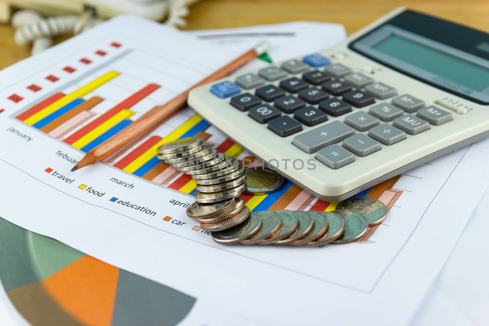 the stack of coin with business paper graphs and pencil with charts report, calculator, concept of calculating expenses, incomes and expenses.