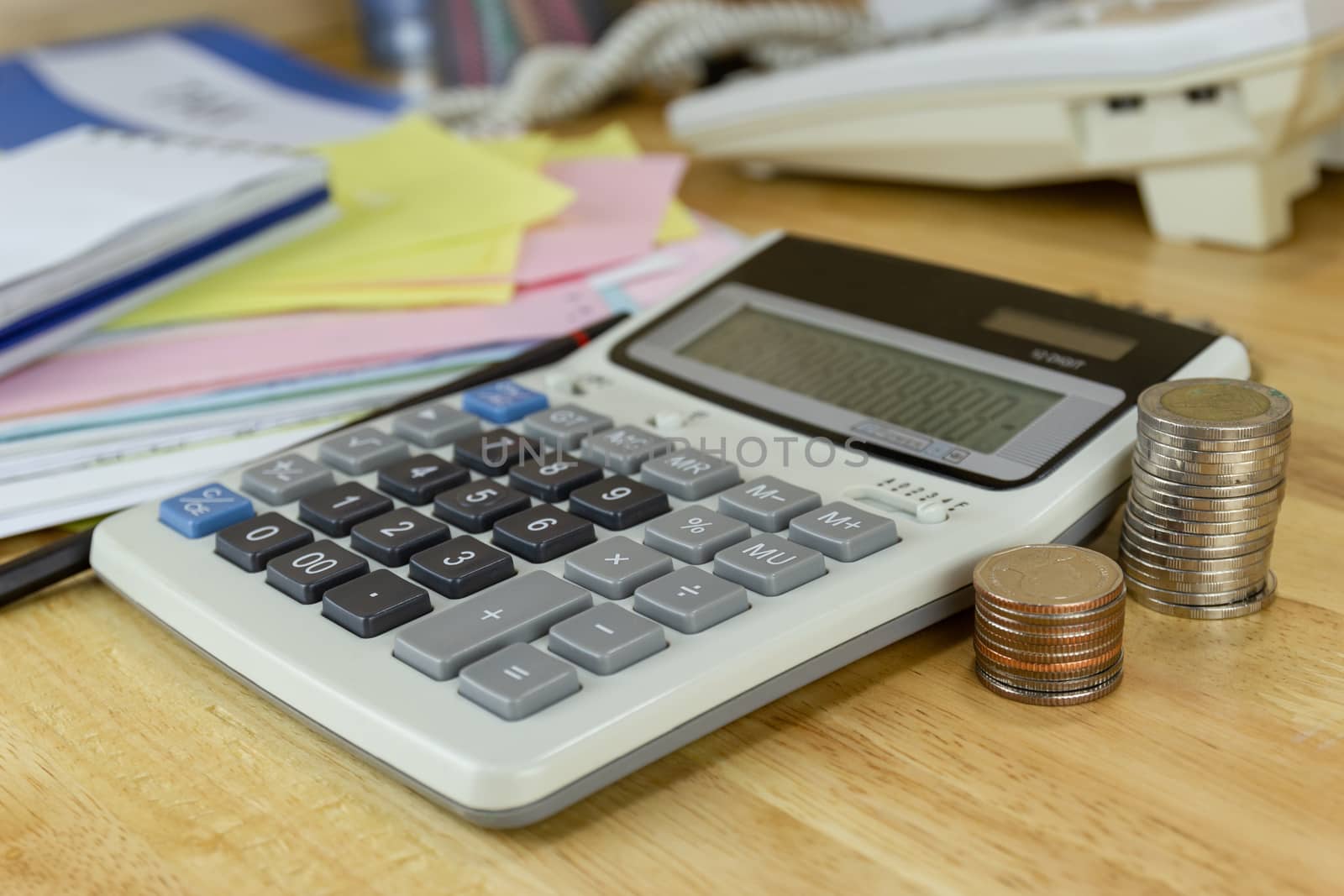 the stack of coin with calculator on wood table at office, concept of calculating expenses, incomes and expenses.