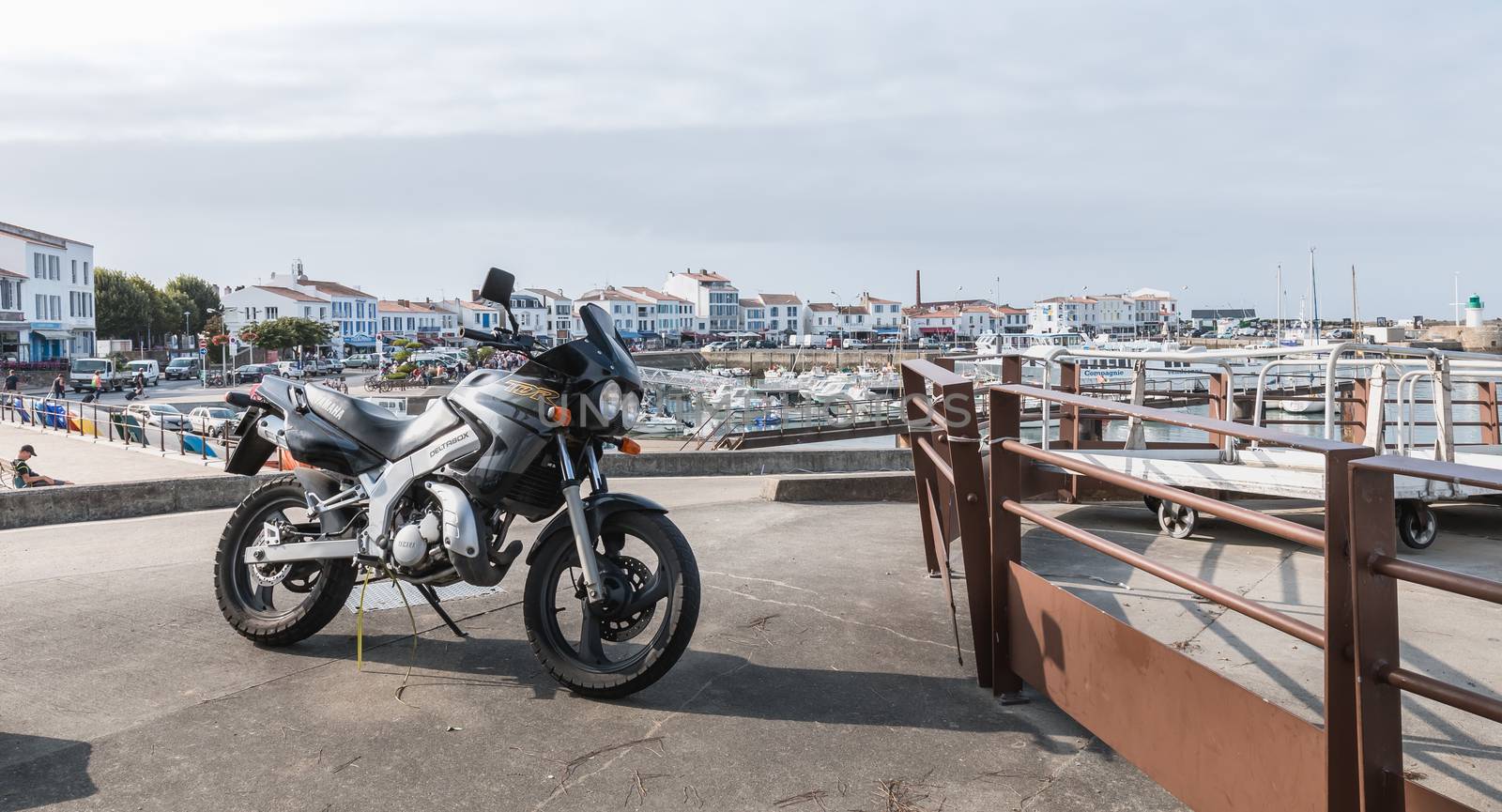 Yeu island, France - September 18, 2018: Motorcycle parked in harbor port Joinville near boats on a summer day