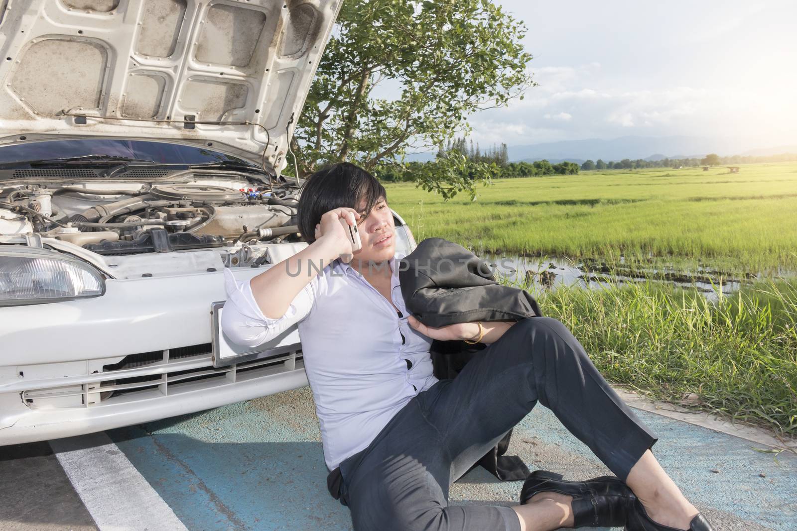 Young asian business man has Broken Down car and sitting calling for help