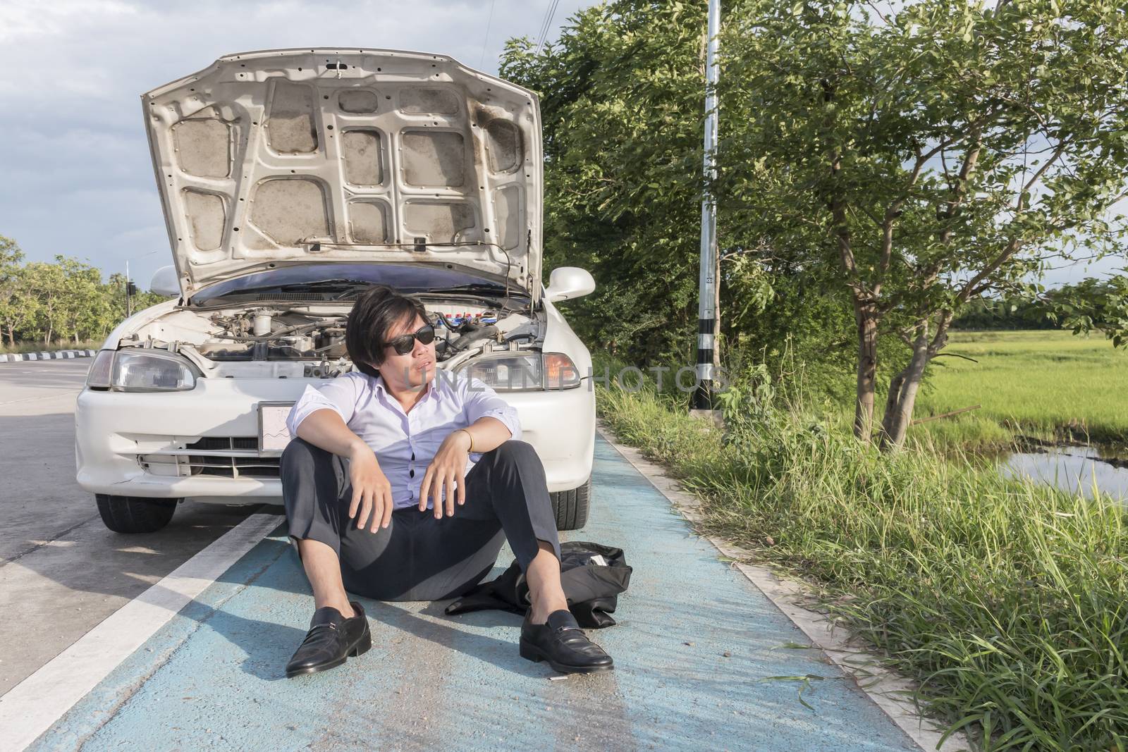 Asian business man sitting on a broken car